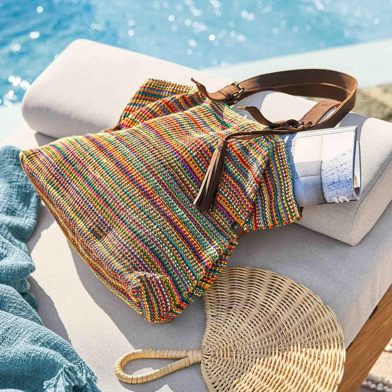 Bunte gewebte Tasche mit braunem Lederhenkel auf hellem Polster am Pool liegend
