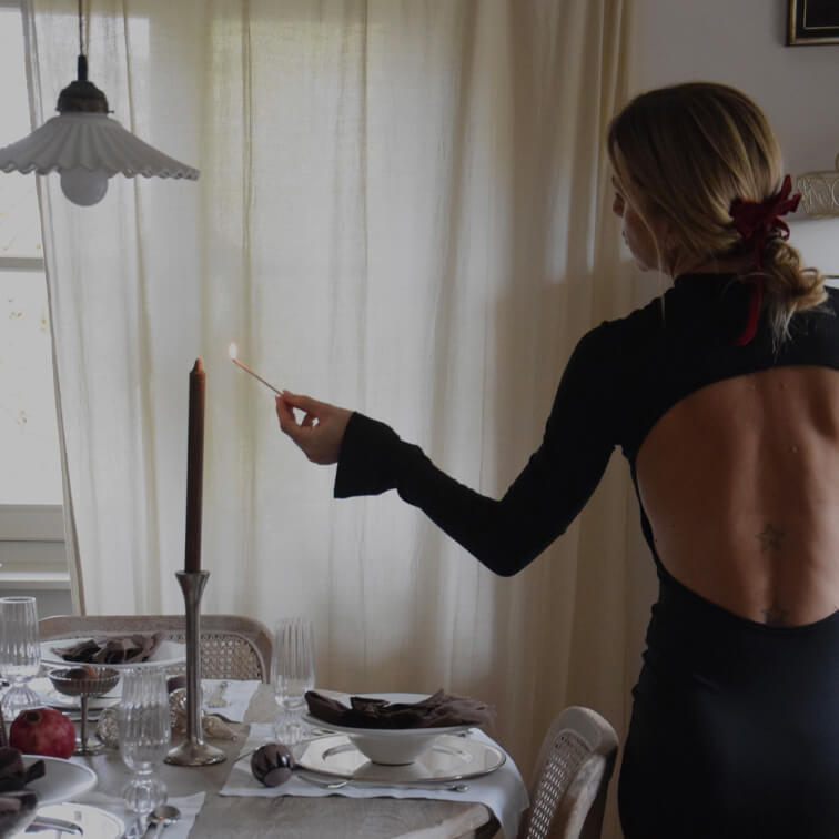 Frau im schwarzen Rückenfreien Kleid zündet Kerze an einem elegant gedeckten Esstisch an