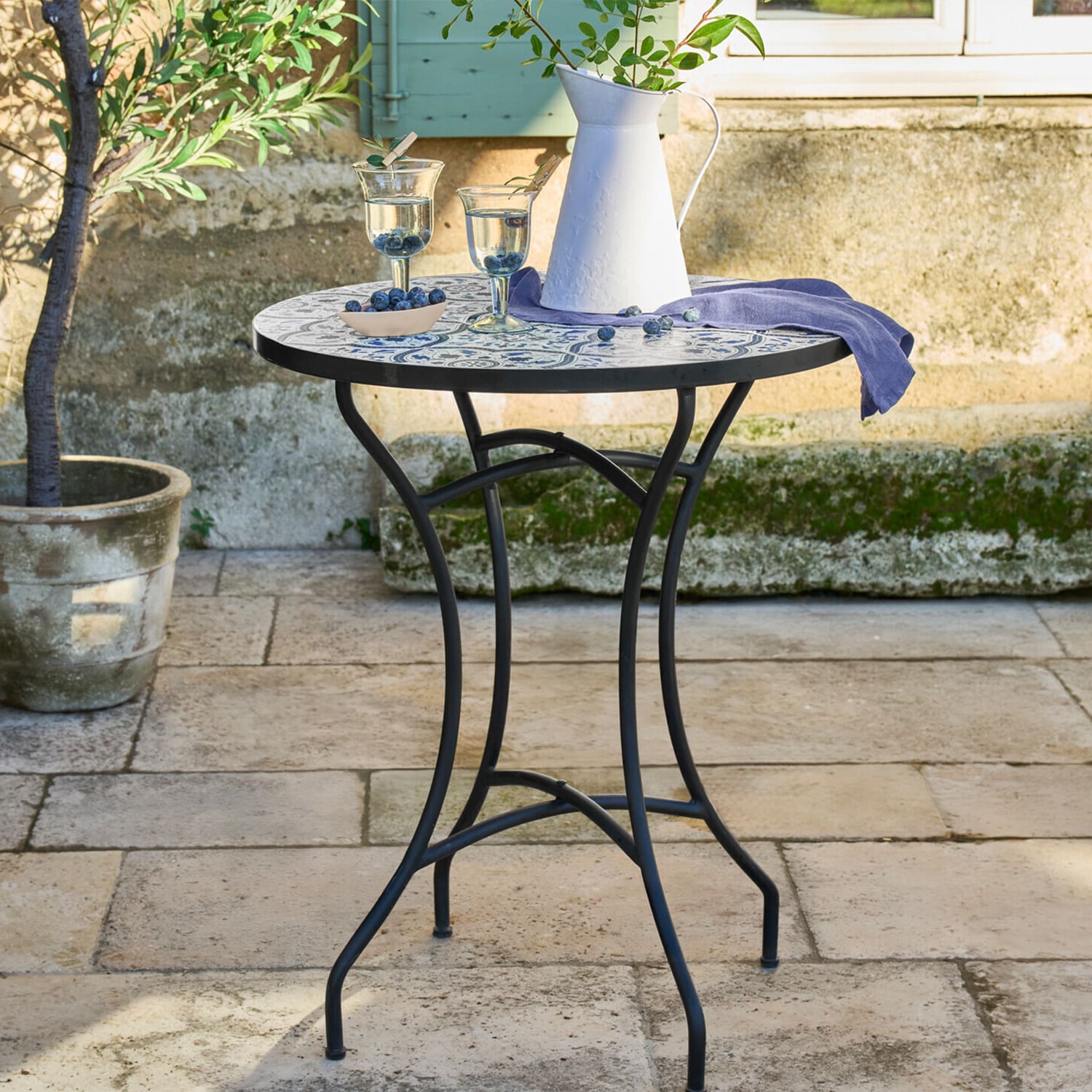 Runder Gartentisch mit schwarzem Metallgestell und blau-weißem Mosaik-Tischplatte im Außenbereich