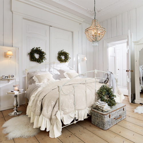 Gemütliches Schlafzimmer mit weißem Metallbett, beiger Bettwäsche, Wanddekorationen und hellem Holzboden