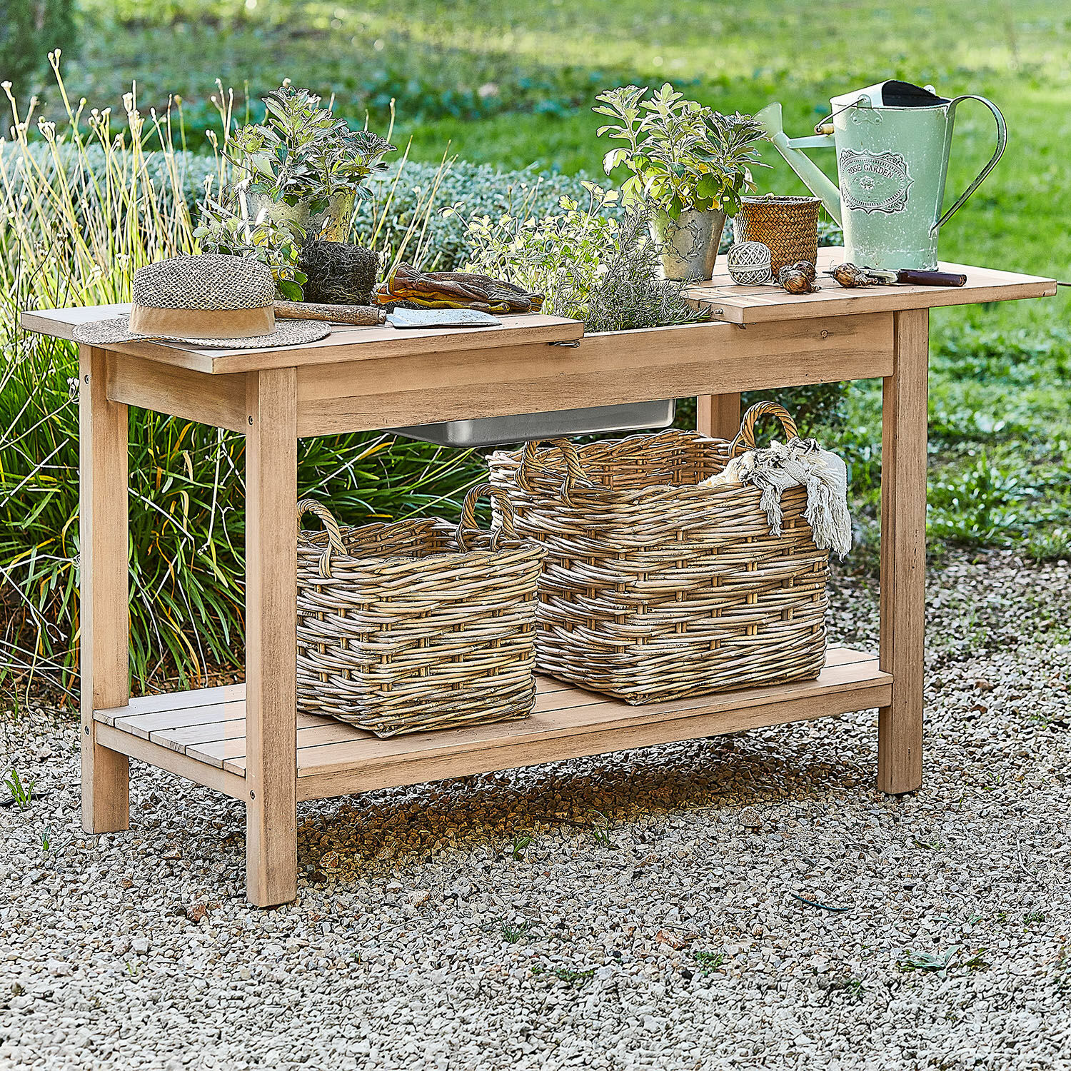 Pflanztisch FSC®-100% Venzone Gartentisch aus Holz mit Pflanztöpfen, grüner Gießkanne und Weidenkörben auf Kiesboden