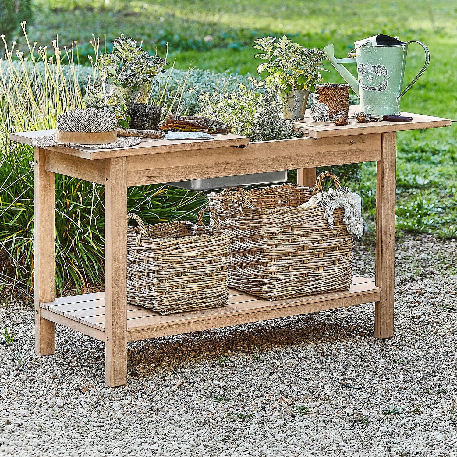 Pflanztisch FSC®-100% Venzone Gartentisch aus Holz mit Pflanztöpfen, grüner Gießkanne und Weidenkörben auf Kiesboden