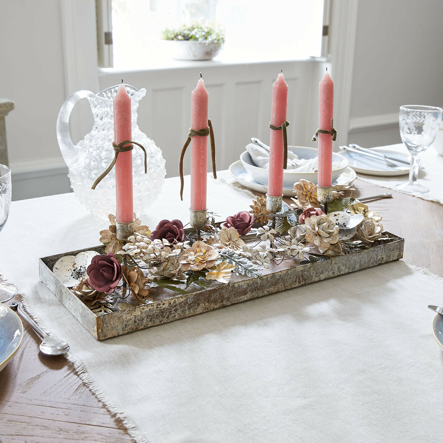 Metall-Kerzenhalter mit vier rosa Kerzen und Blumenverzierung auf dem Esstisch