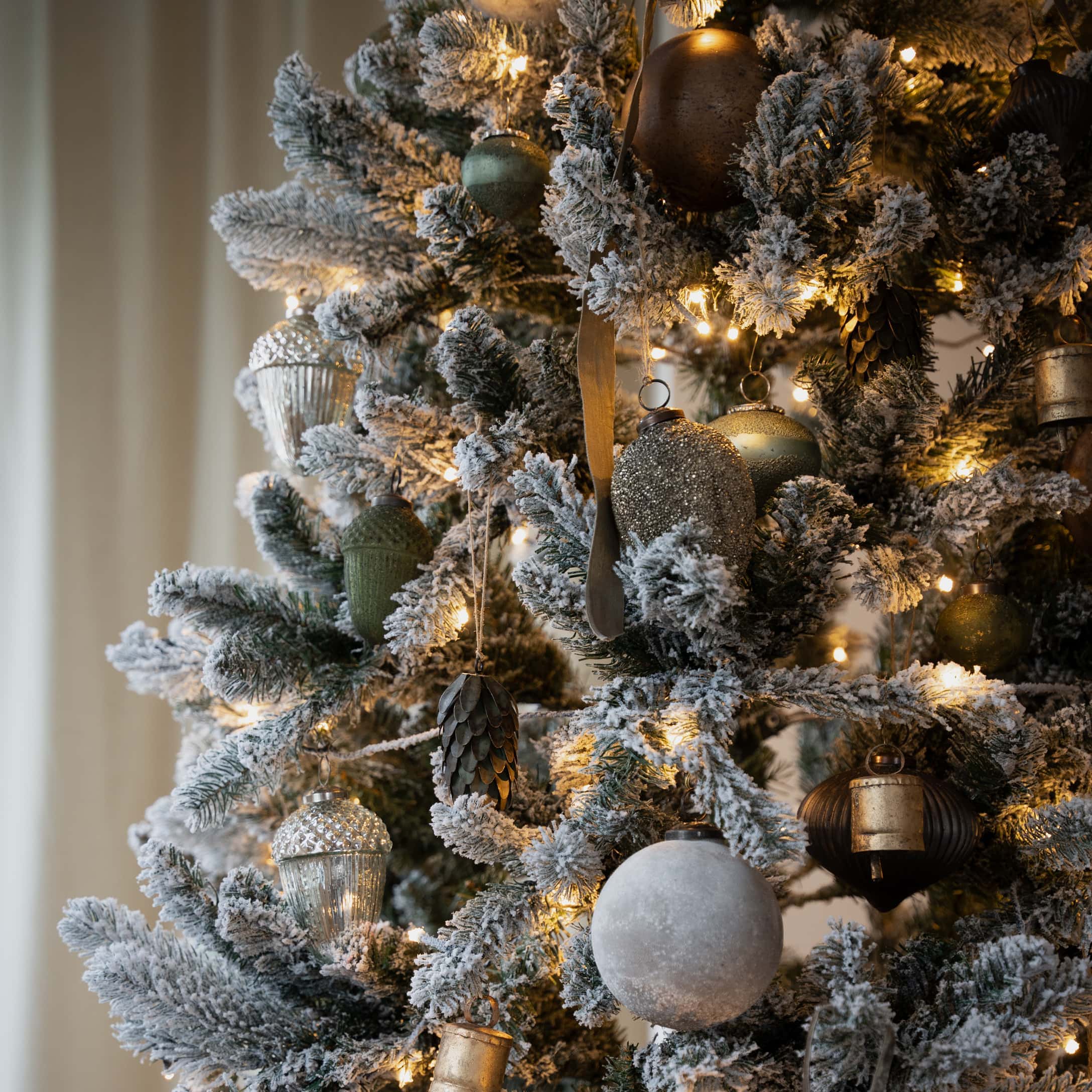 Künstlicher Weihnachtsbaum mit schneebedeckten Zweigen und gold-grünen Christbaumschmuck, festliche Deko