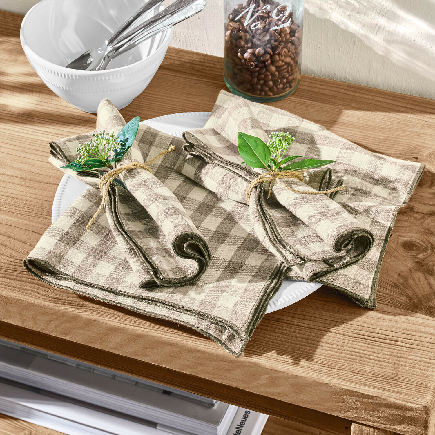 Leinenservietten in Beige-Braun kariert mit grünen Zweigen als Dekoration auf Holztisch