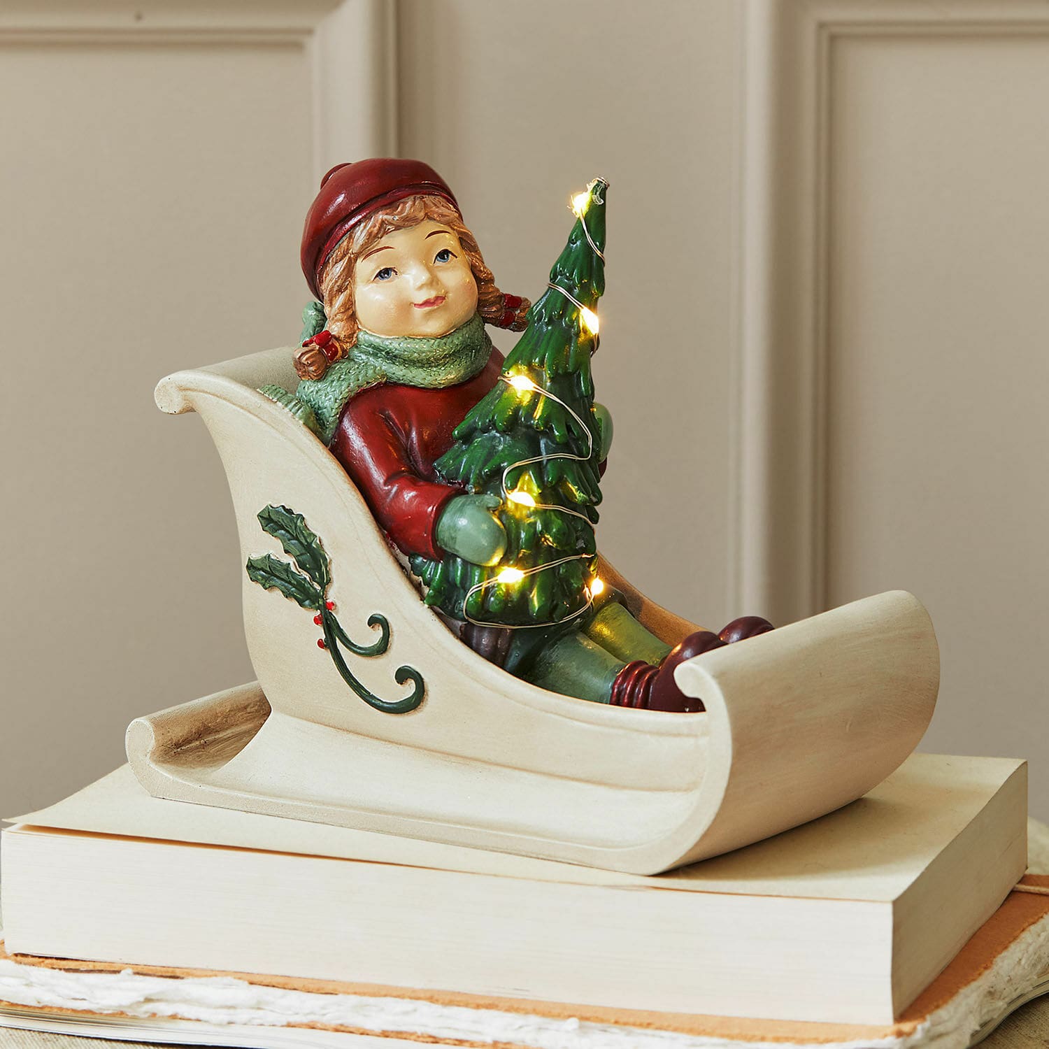 LED-Figur Soriala Kindfigur im Schlitten mit grünem Weihnachtsbaum und Lichterkette, festliche Dekoration auf Büchern