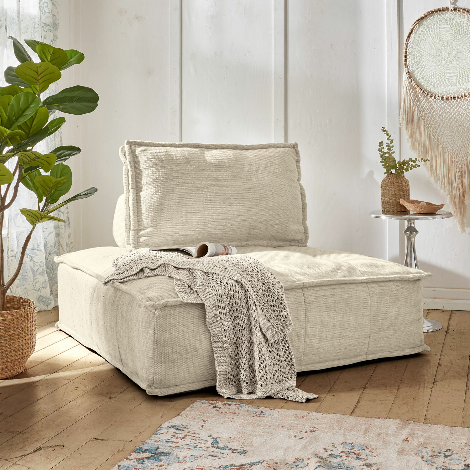 Loungesofa Tesshill Beiger Polstersessel aus Stoff mit weicher Rückenlehne und gestrickter Decke in hellem Wohnzimmer mit Holzboden