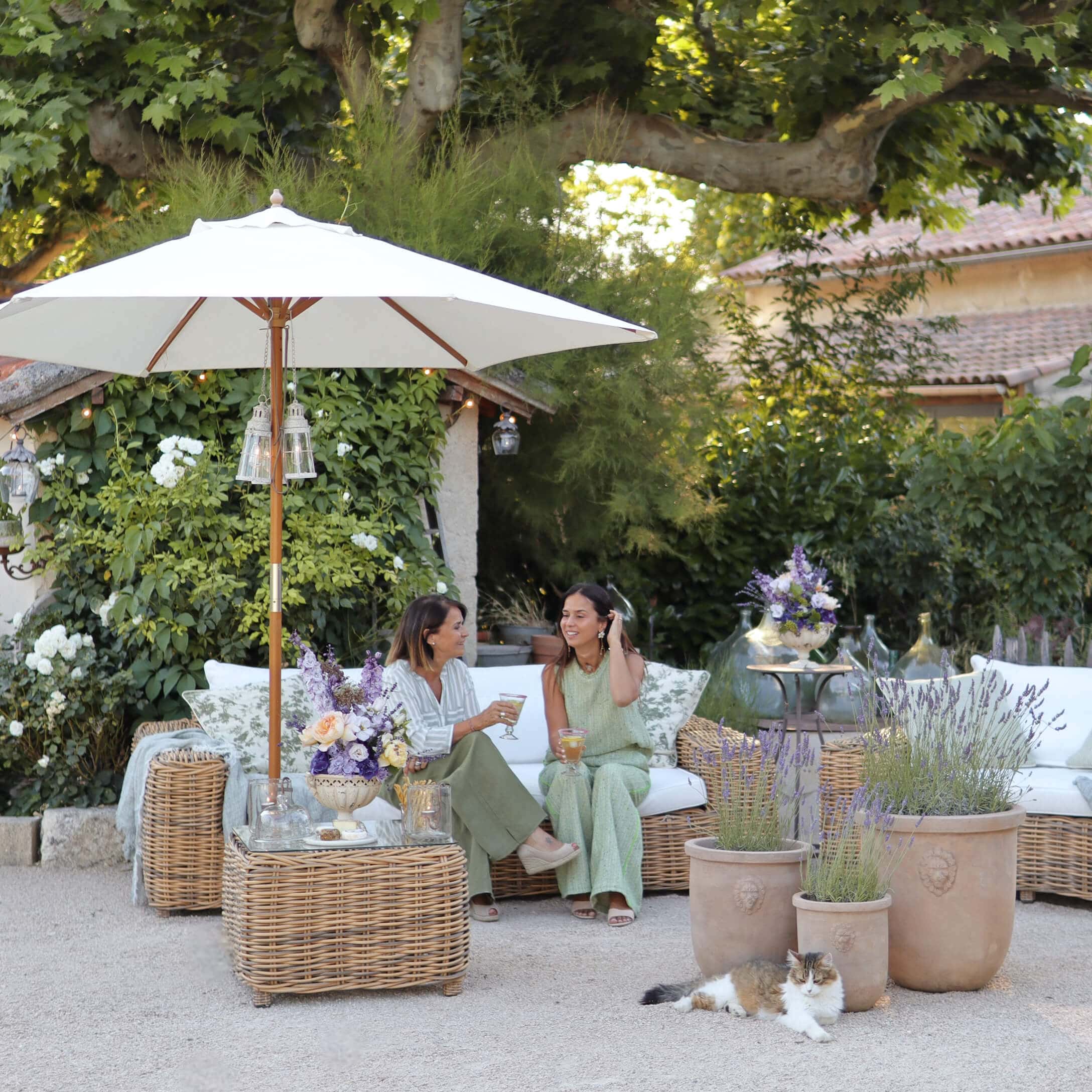 Gartenmöbel aus natürlichem Rattan mit weißen Kissen und Sonnenschirm, dekoriert mit Lavendeltöpfen