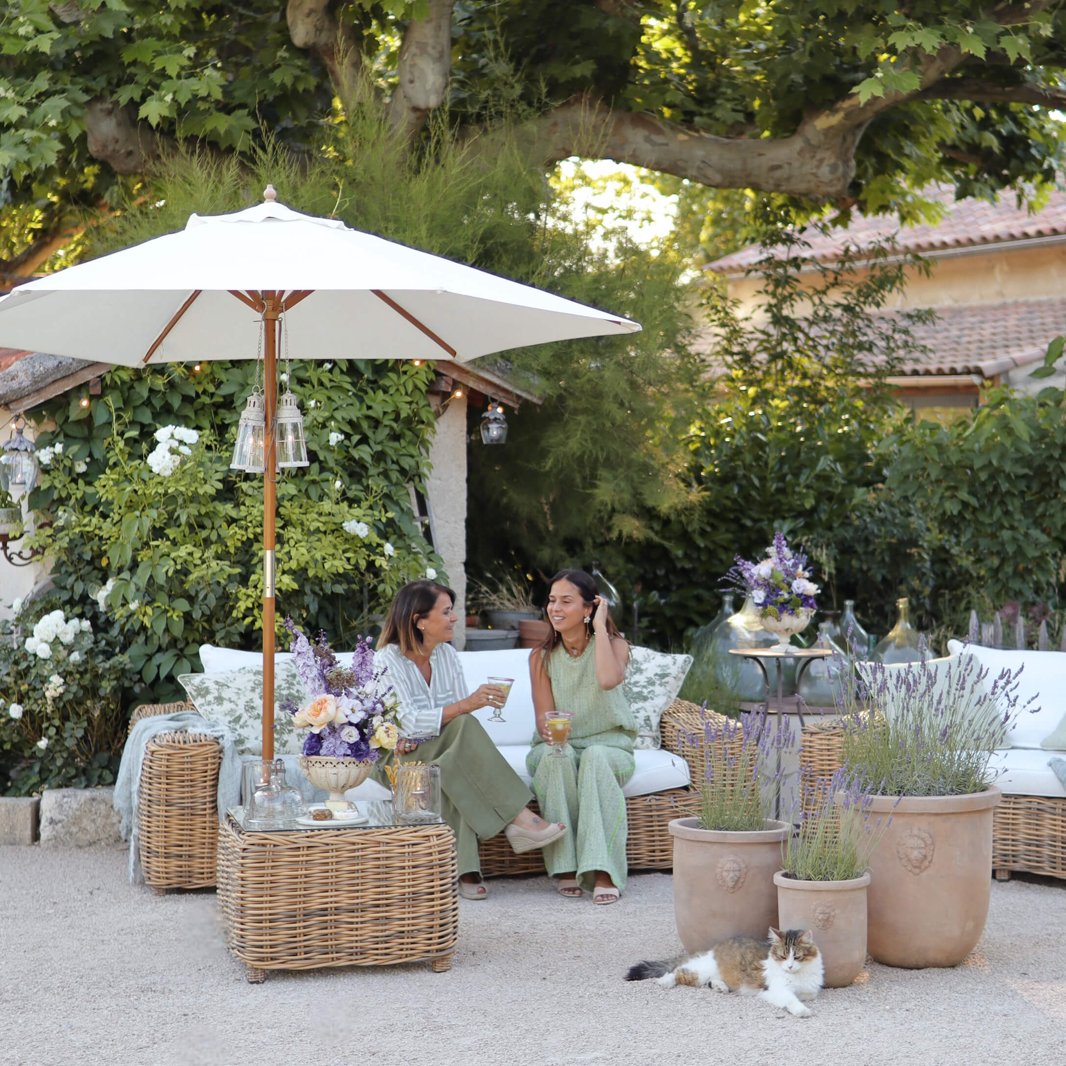Gartenmöbel aus natürlichem Rattan mit weißen Kissen und Sonnenschirm, dekoriert mit Lavendeltöpfen