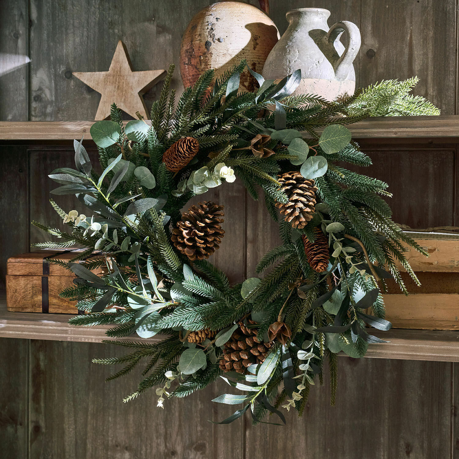 Dekorativer Weihnachtskranz mit grünen Zweigen und Zapfen auf rustikalem Holzregal