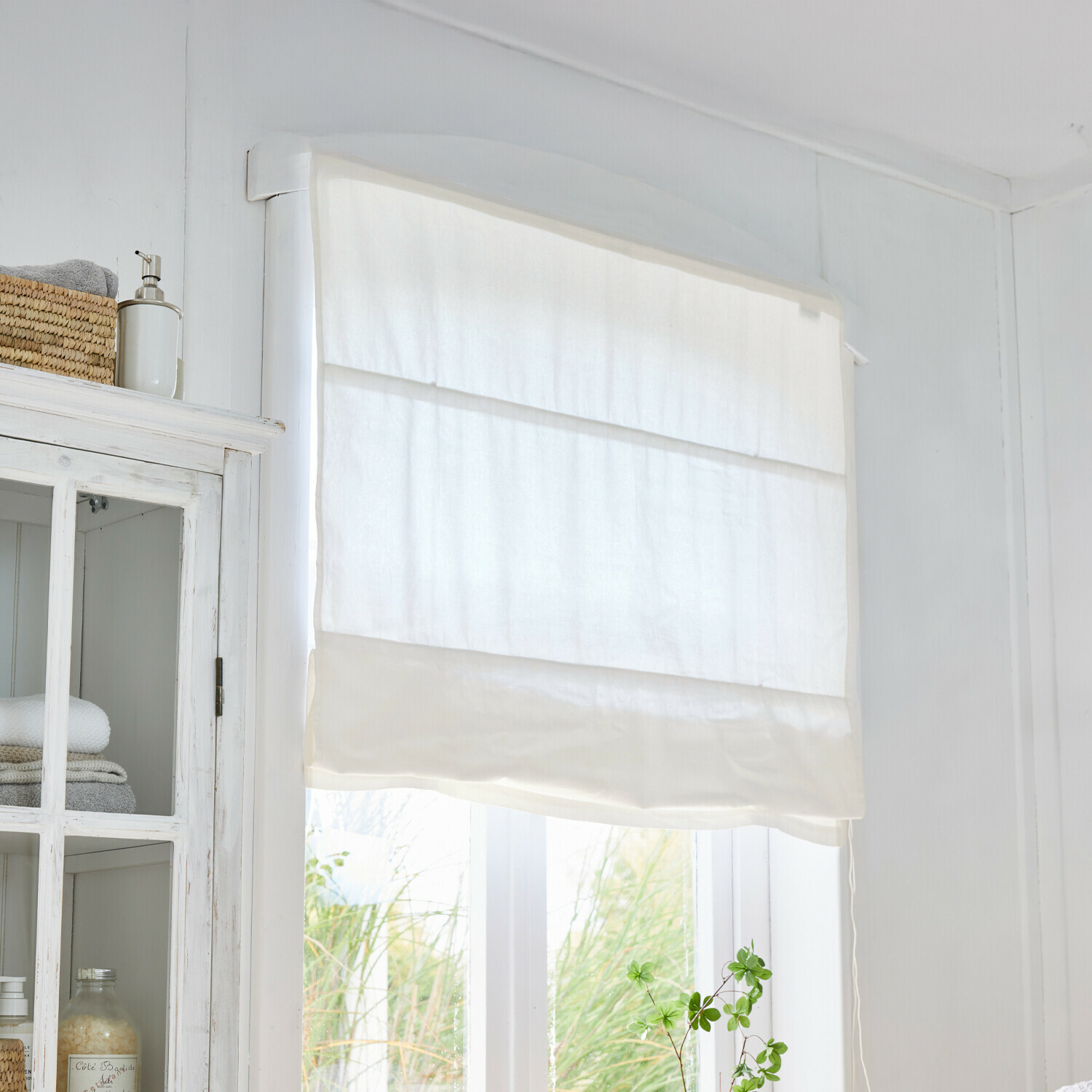 Weiße römische Jalousie aus leichtem Stoff in hellem Raum mit Pflanze am Fenster