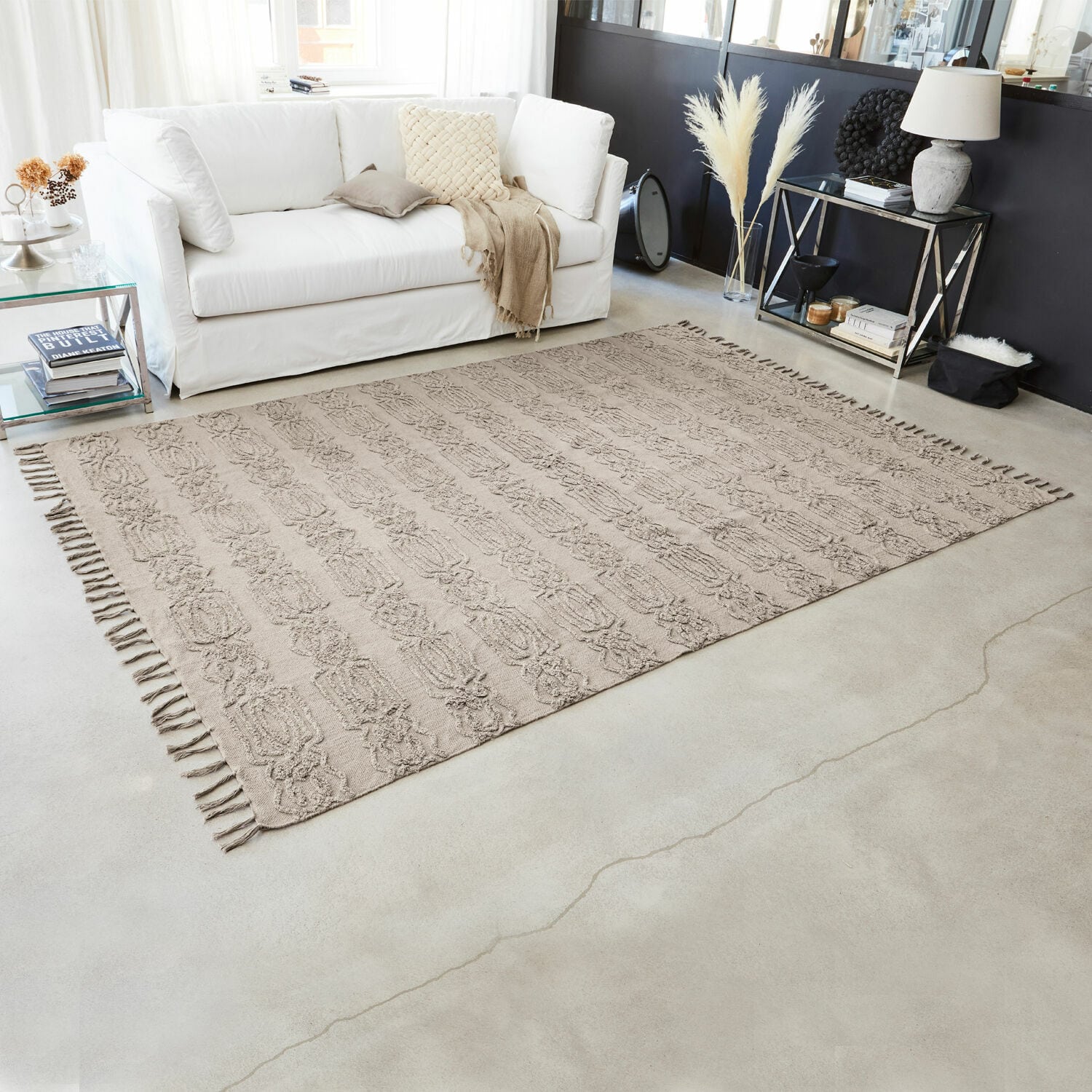 Beiger Baumwollteppich mit Fransen und Muster in modernem Wohnzimmer mit weißem Sofa und Dekorationen