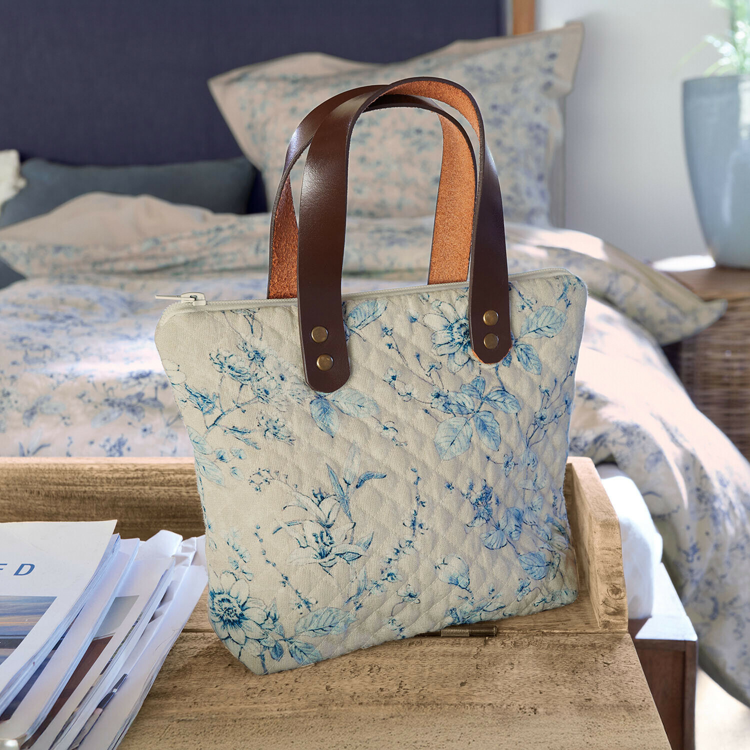 Tasche Vailenne Beige gesteppte Tasche mit blauem Blumenmuster und braunen Ledergriffen auf Holztisch