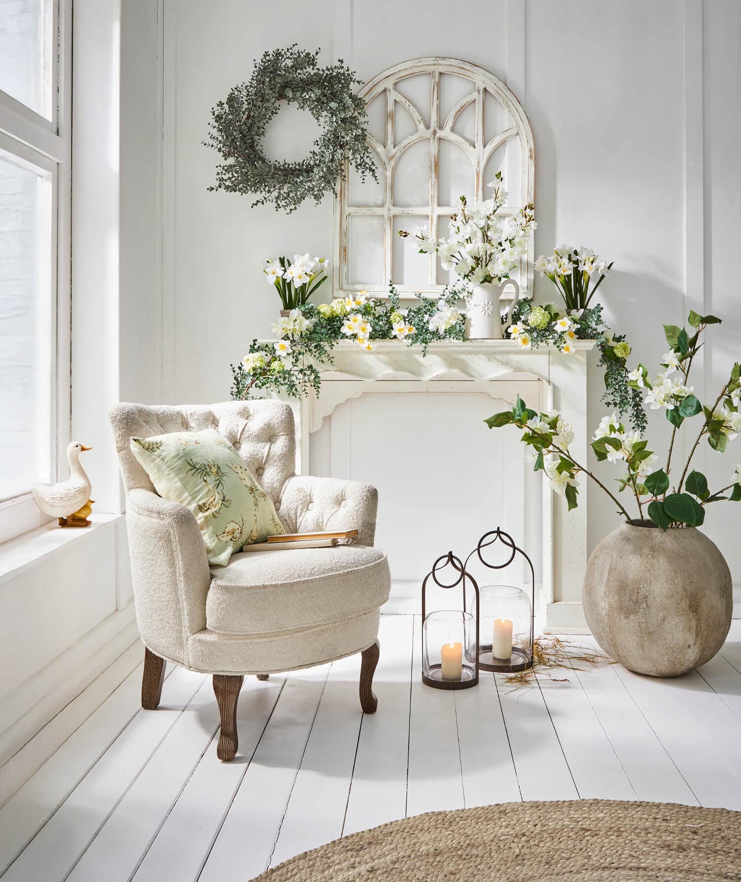 Beiger Polsterstuhl mit Kissen neben dekorativem Kaminsims mit Blumen und Laternen in hellem Raum