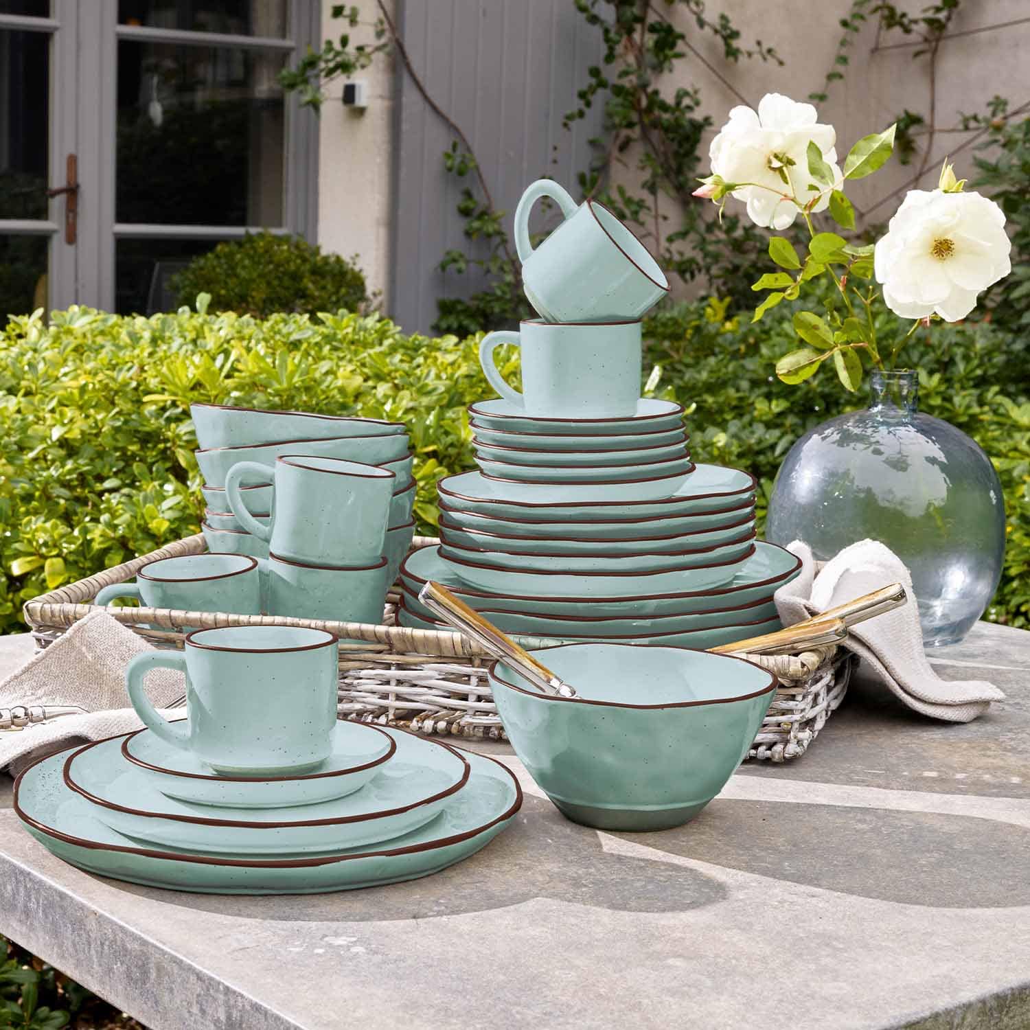 Mintgrünes Keramik-Geschirrset mit braunem Rand auf Gartentisch arrangiert