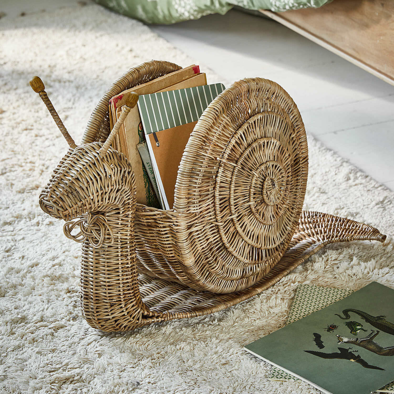 Korb Tigrelle Wiklinener Bücherhalter in Schneckenform in Naturfarbe auf hellem Teppich für Wohnaccessoires