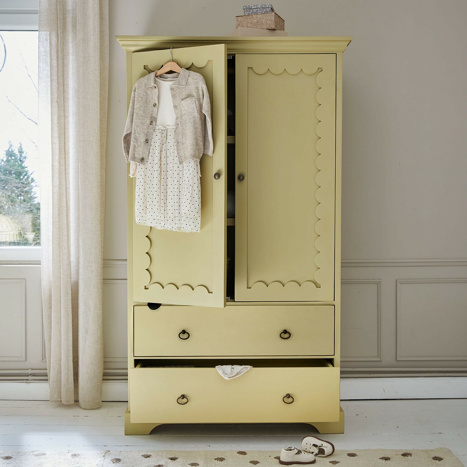 Kinderkleiderschrank Frollin Gelber Holzschrank mit dekorativen Türen und Kinderkleidung an der Tür in hellem Raum