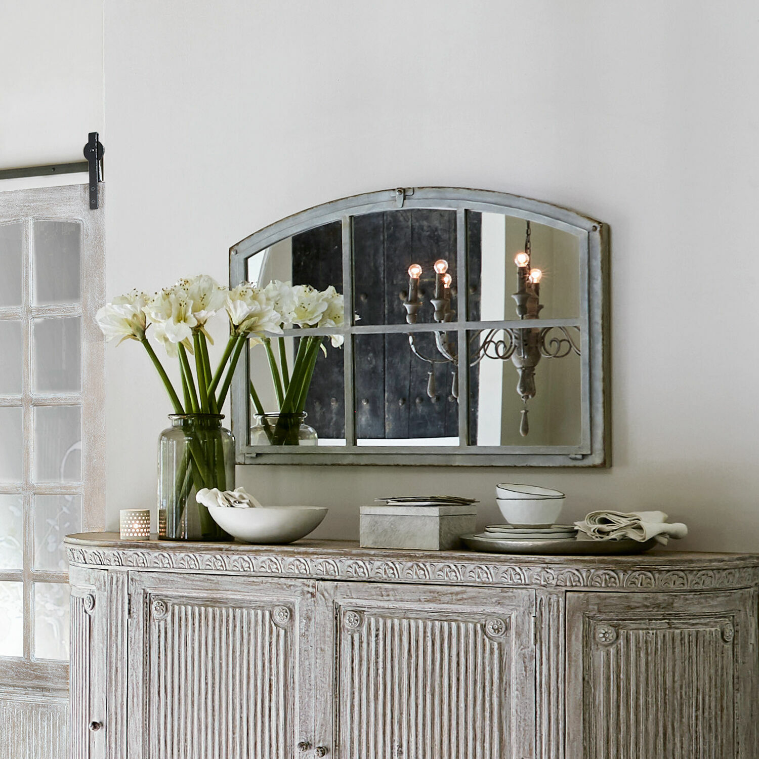 Rustikaler weiß gewaschener Holzschrank mit Spiegel und Dekorationen auf der Ablage in hellem Raum