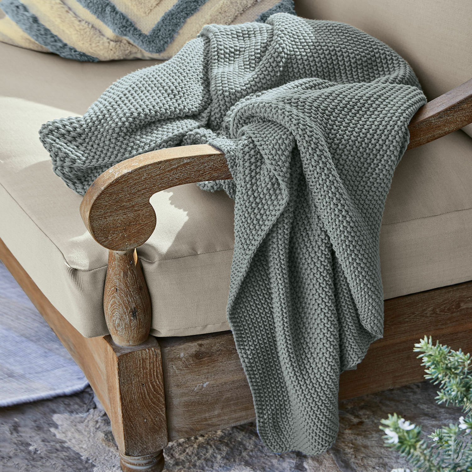 Plaid Ancy Grau gestrickte, dicke Decke aus weicher Wolle auf einem Holzstuhl mit beigem Polster