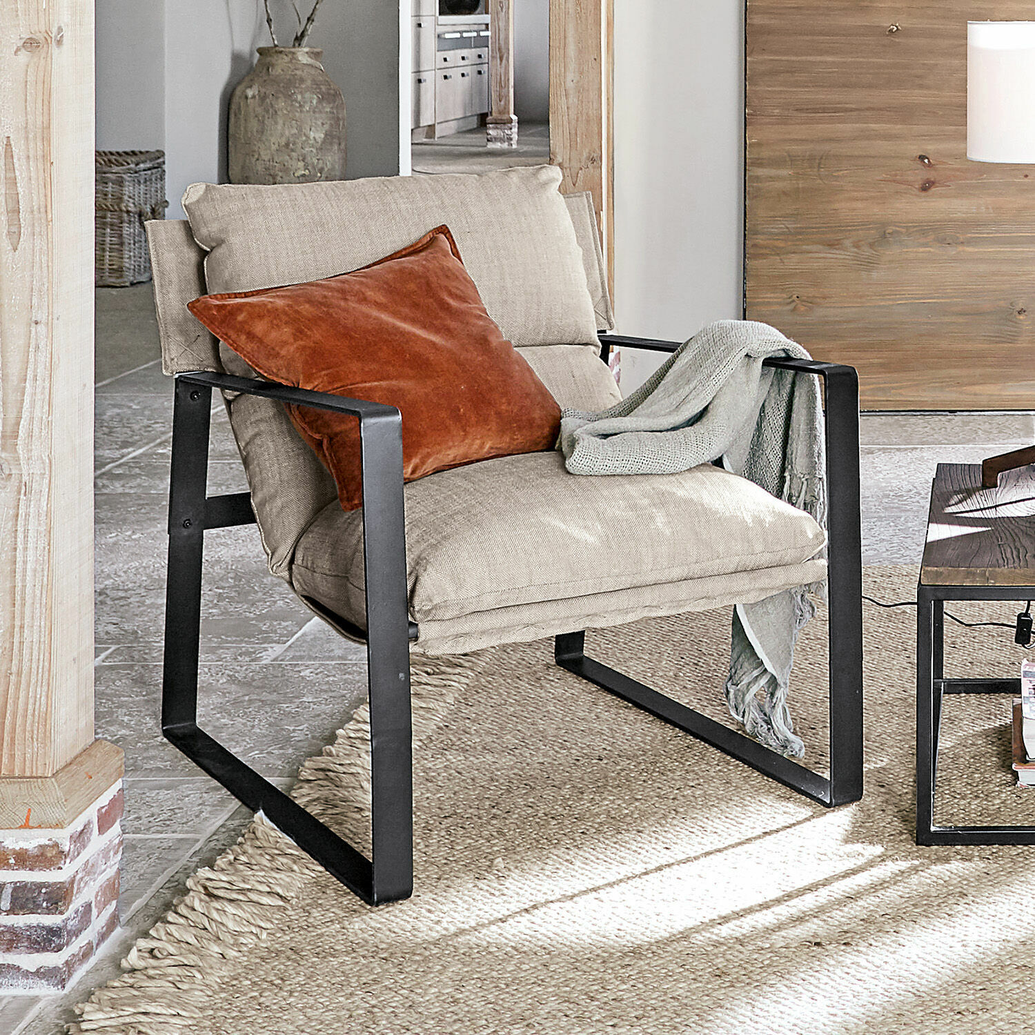 Sessel Seuvard Beiger Polsterstuhl mit schwarzem Metallgestell, orangefarbener Kissen und grauem Plaid im Wohnzimmer