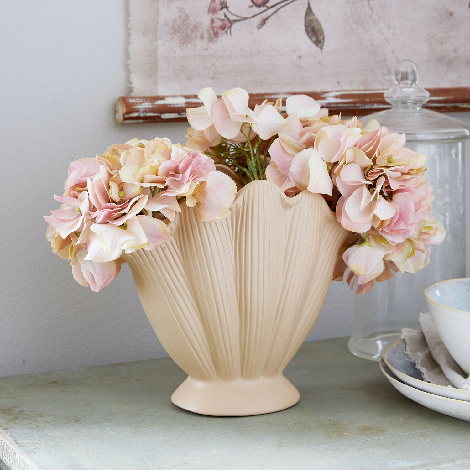 Beige Keramikvase mit Blattstruktur und rosa Dekoblumen auf einem Tisch