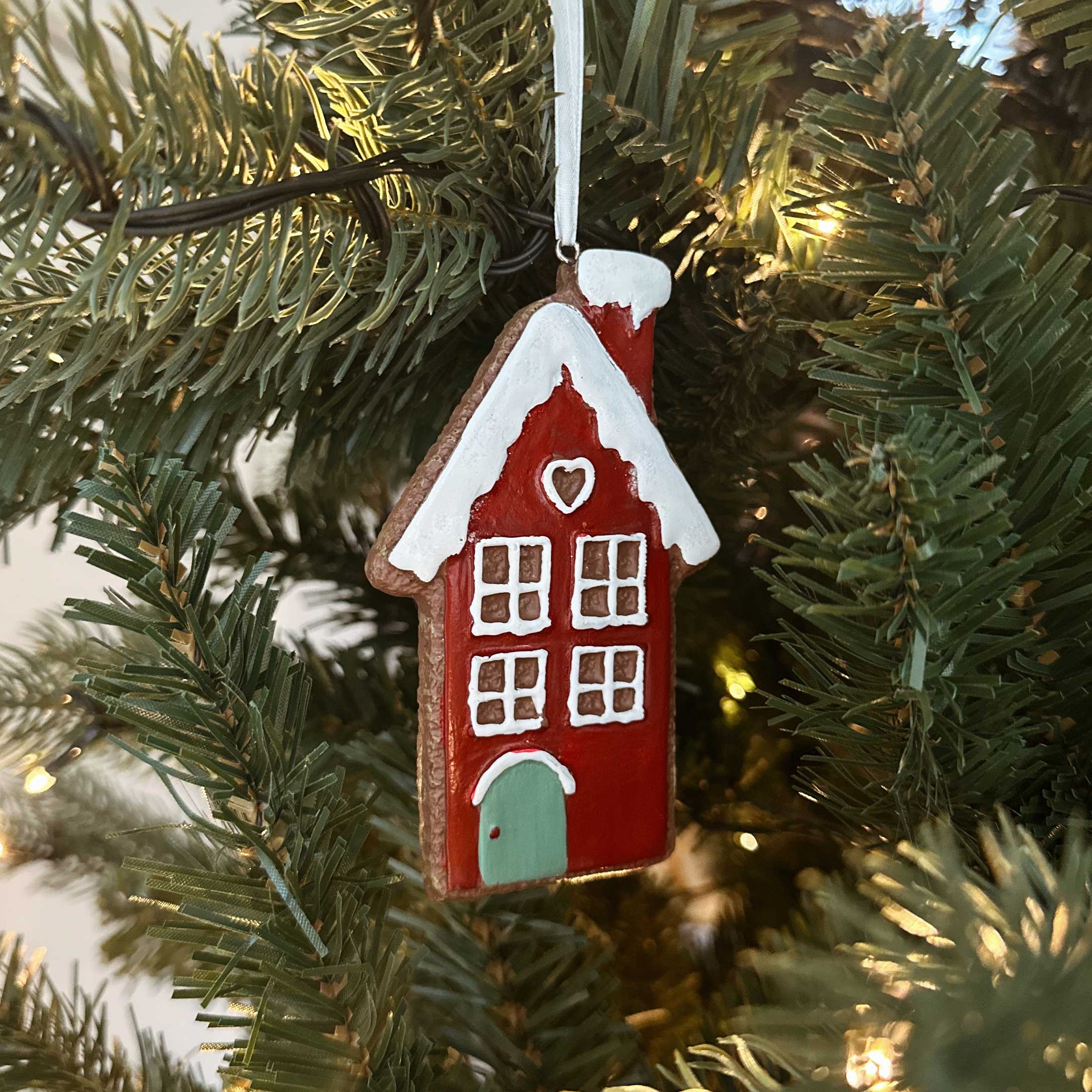 Rotes Keramik-Weihnachtshaus mit weißem Dach und grüner Tür als Baumdekoration am Tannenbaum