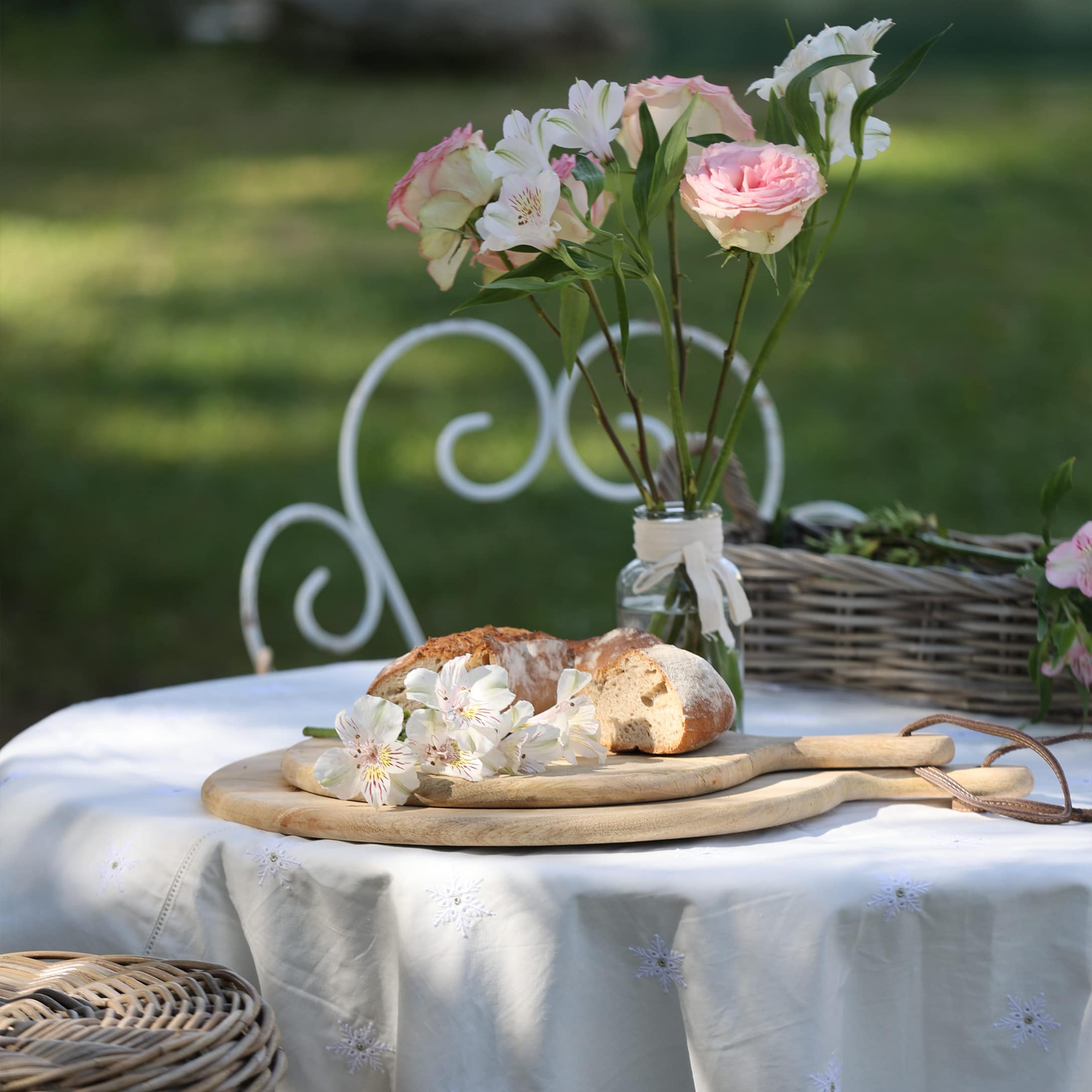 Holz-Schneidebretter mit Brot und Blumen auf weißer Tischdecke im Garten