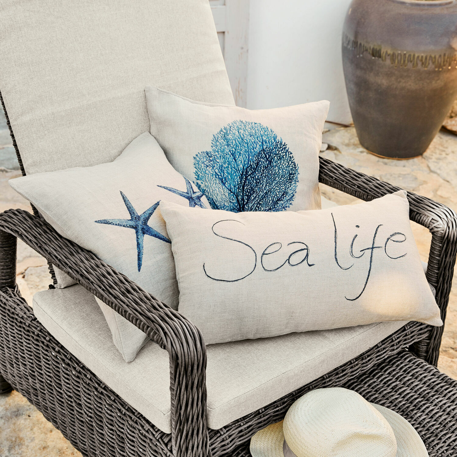 Kissenhülle 3er Set Sea life Beige Leinenkissen mit maritimen Motiven auf grauem Rattansessel auf Terrasse