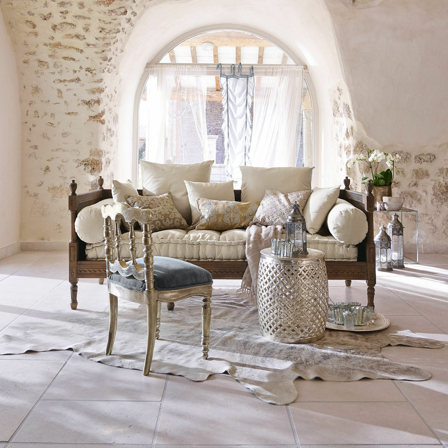 Gemütliches Wohnzimmer mit Holzsofa, cremefarbenen Kissen, silbernem Beistelltisch und blauem Samtstuhl