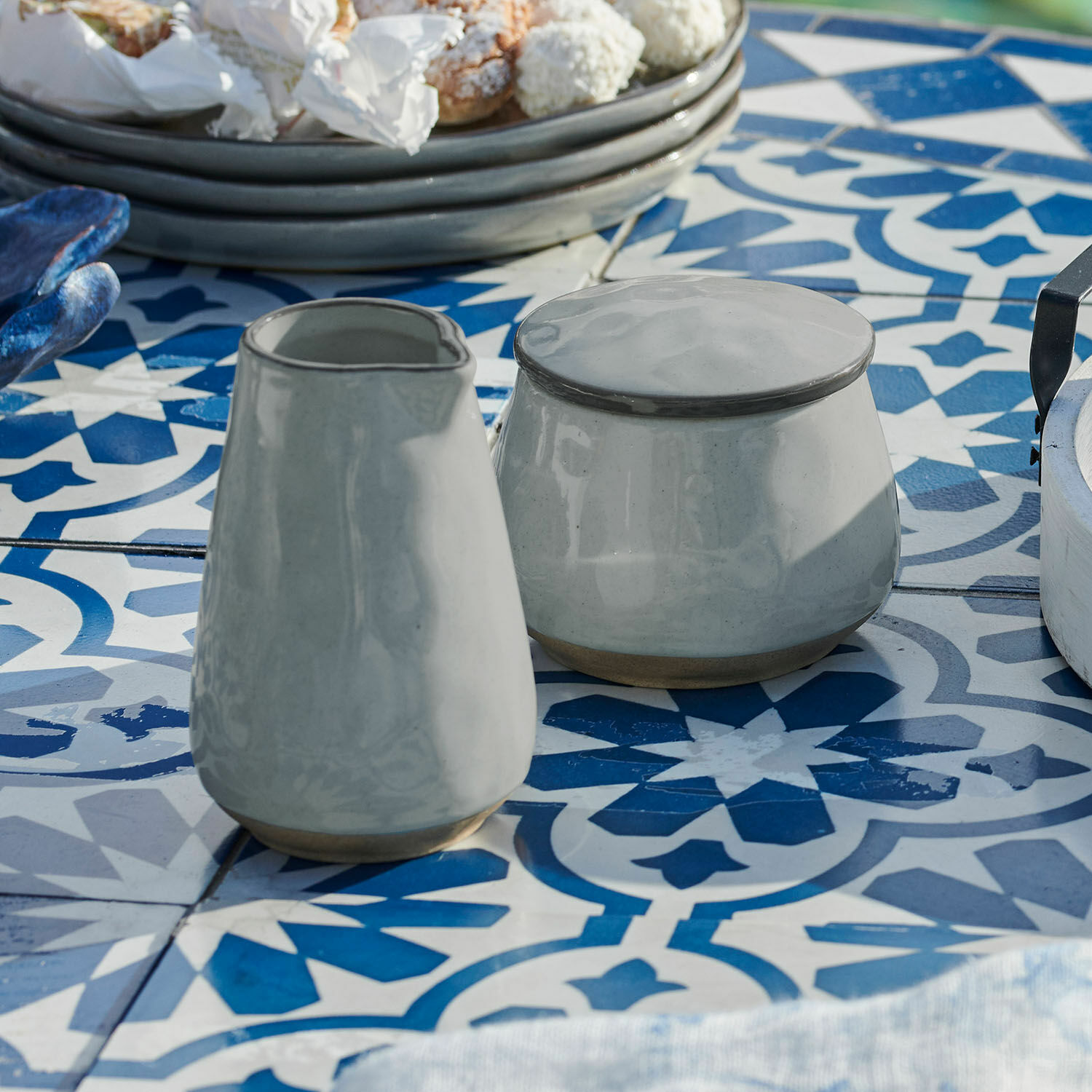 Zuckerdose und Milchkännchen Biarré Graue Keramik-Zuckerdose und Milchkännchen auf blau-weiß gemustertem Esstisch