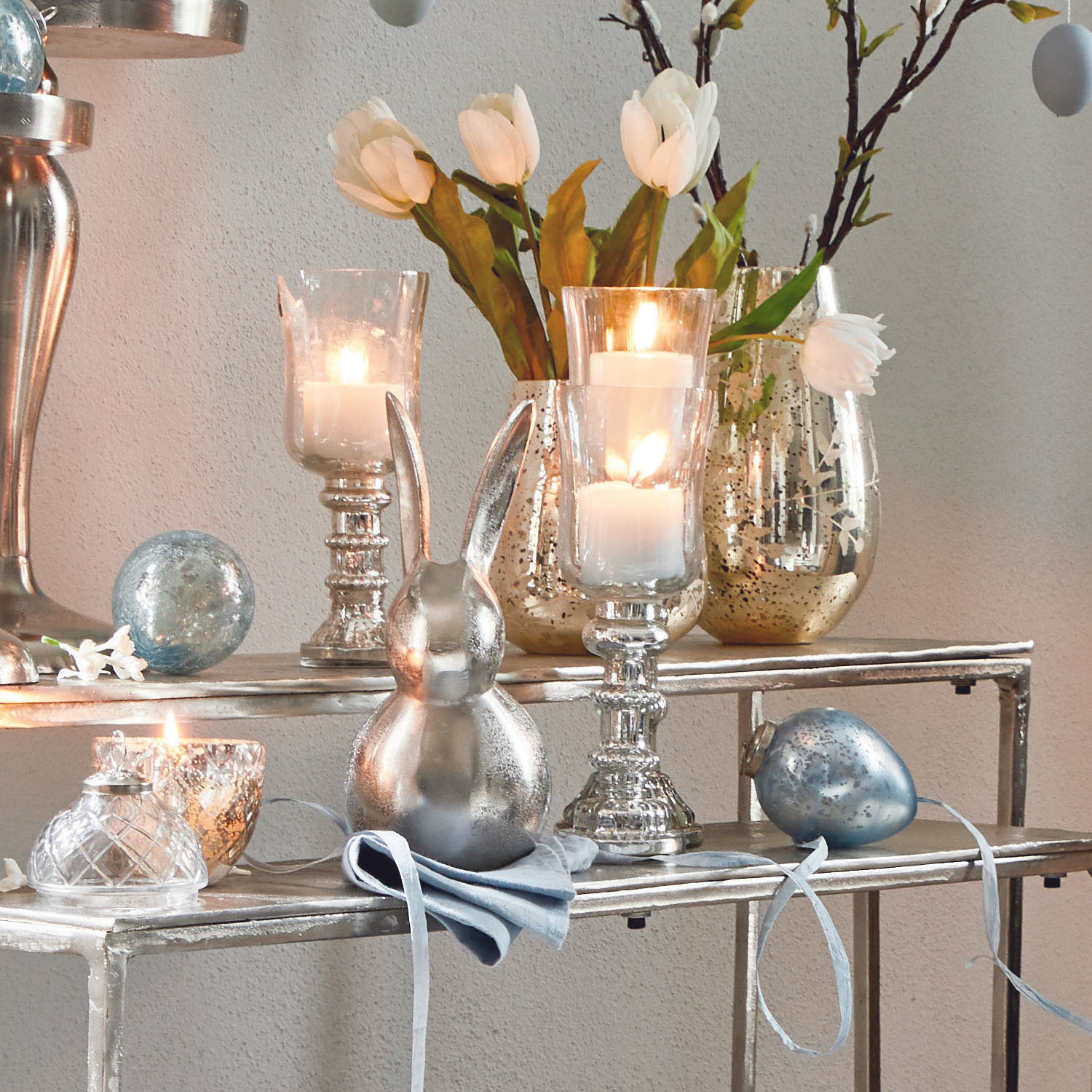 Dekorativer silberner Hase und Glas-Kerzenhalter mit weißen Tulpen auf Metallregal