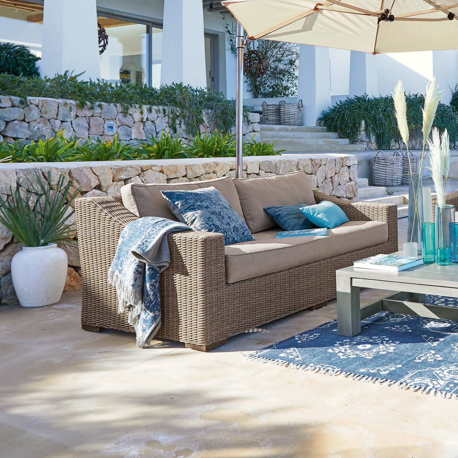 Sofa Chestingdale Beiges Rattan-Gartensofa mit blauen Kissen und Sonnenschirm auf sonniger Terrasse