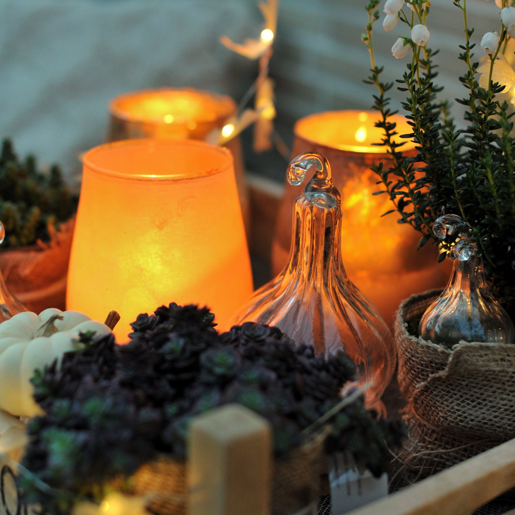 Herbstliche Dekoration mit gläsernen Kürbissen und orangefarbenen Kerzen für gemütliche Stimmung