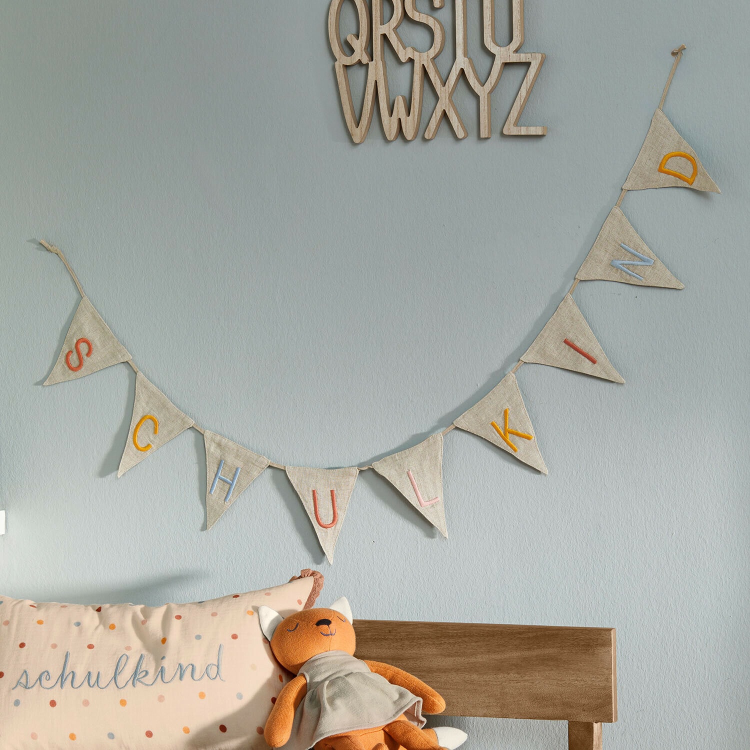 Stoffgirlande mit bunten Buchstaben SCHULKIND an hellblauer Wand im Kinderzimmer