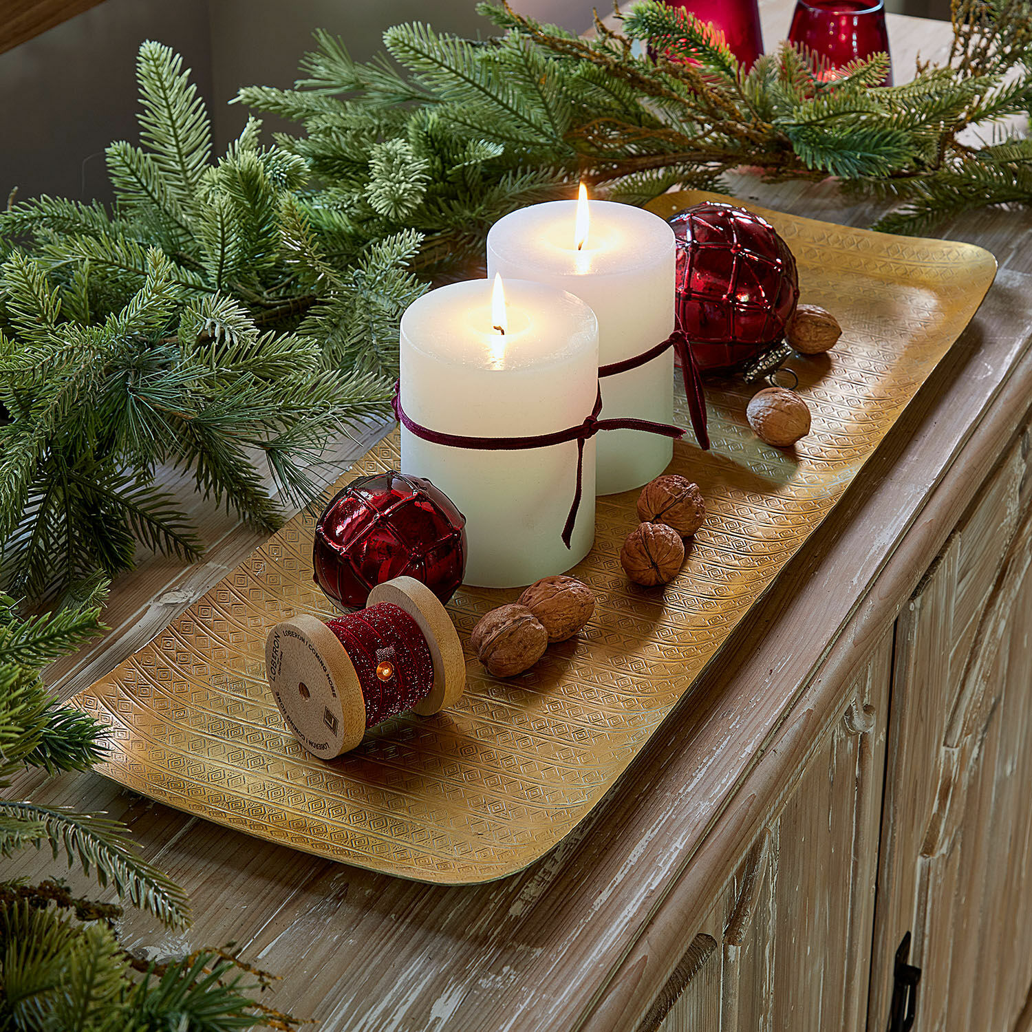 Goldene Metallplatte mit weißen Kerzen, roten Dekokugeln und Walnüssen auf Holzkommode, Weihnachtsdeko