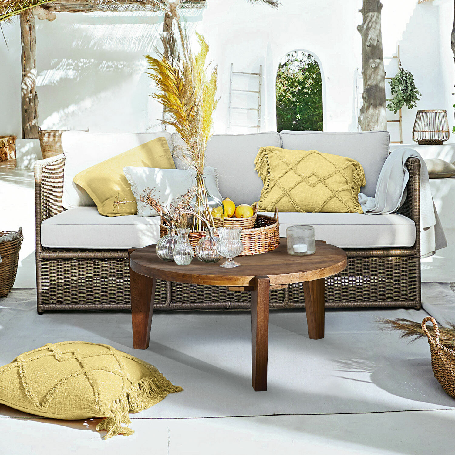 Sofa Lesmont Wohnbereich mit Rattansofa, hellgrauen Kissen und runder Holzcouchtisch auf sonniger Terrasse