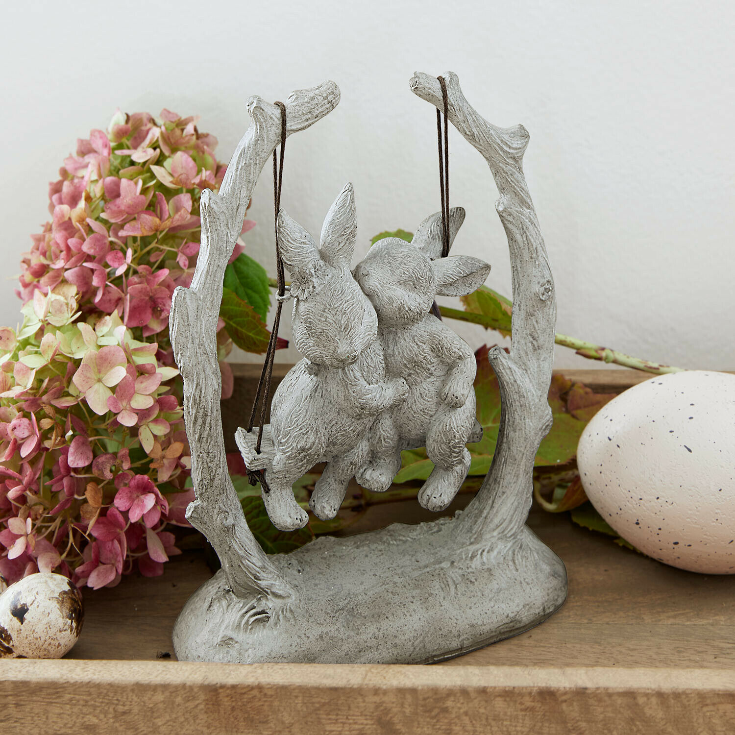 Graue Steinskulptur mit zwei Hasen auf Schaukel, dekorative Osterfigur