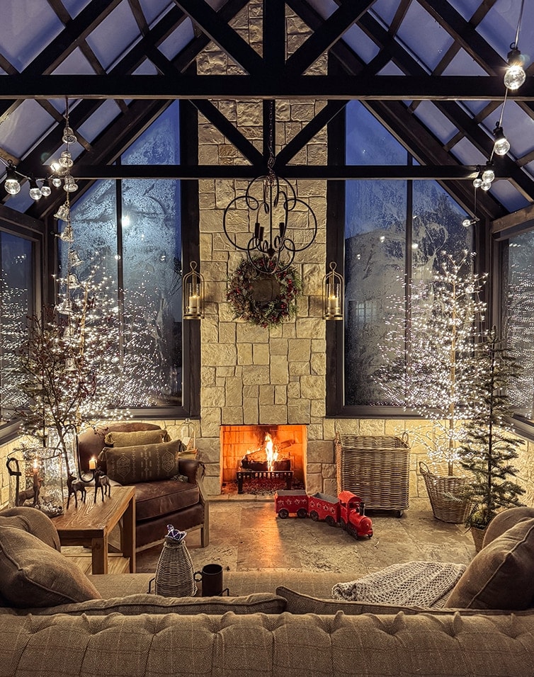 Gemütliches Wohnzimmer mit Kamin, Weihnachtsdekoration und beleuchteten Bäumen in der Orangerie.