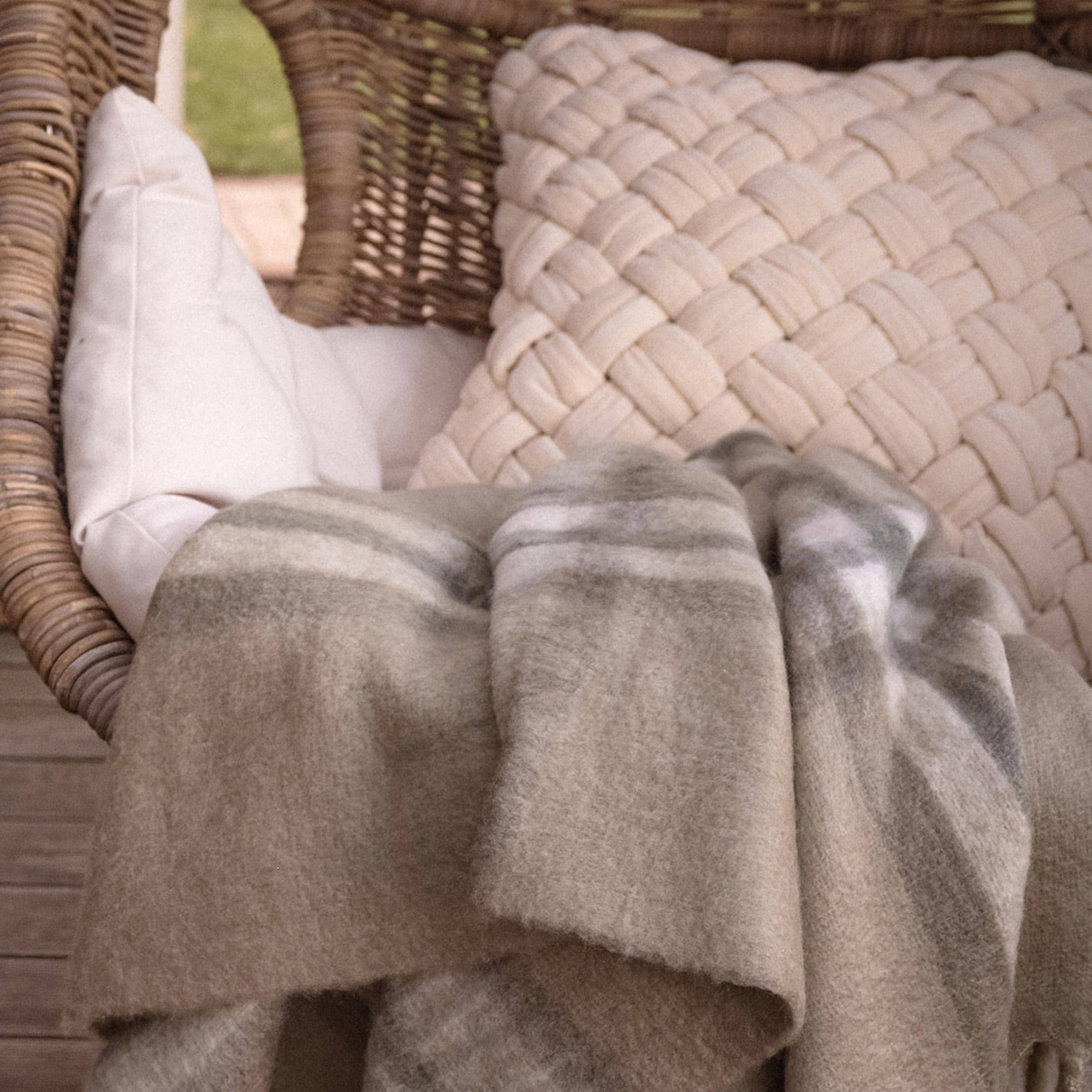 Beiger weicher Plaid mit dezentem Muster auf Rattansessel mit Kissen auf Terrasse
