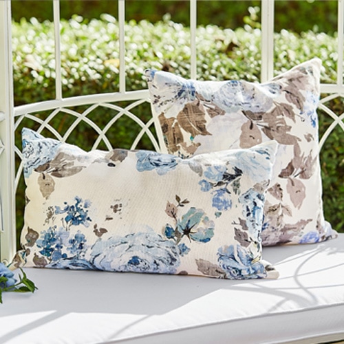 Dekorative Kissen mit blau-beigem Blumenmuster auf weißer Gartenbank aus Metall