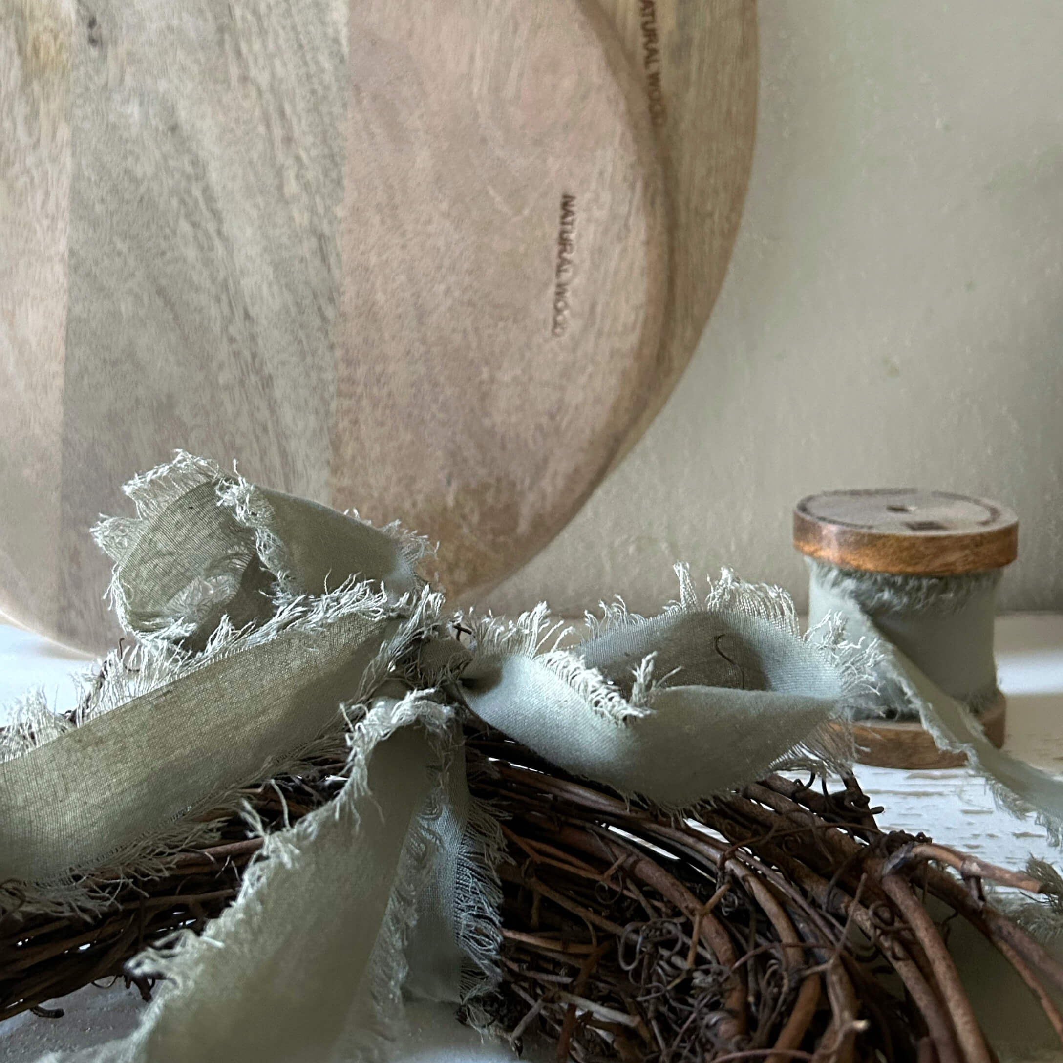 Natürlicher Holzteller mit grauem Leinenband auf einem Weidenkranz als Wohnaccessoire