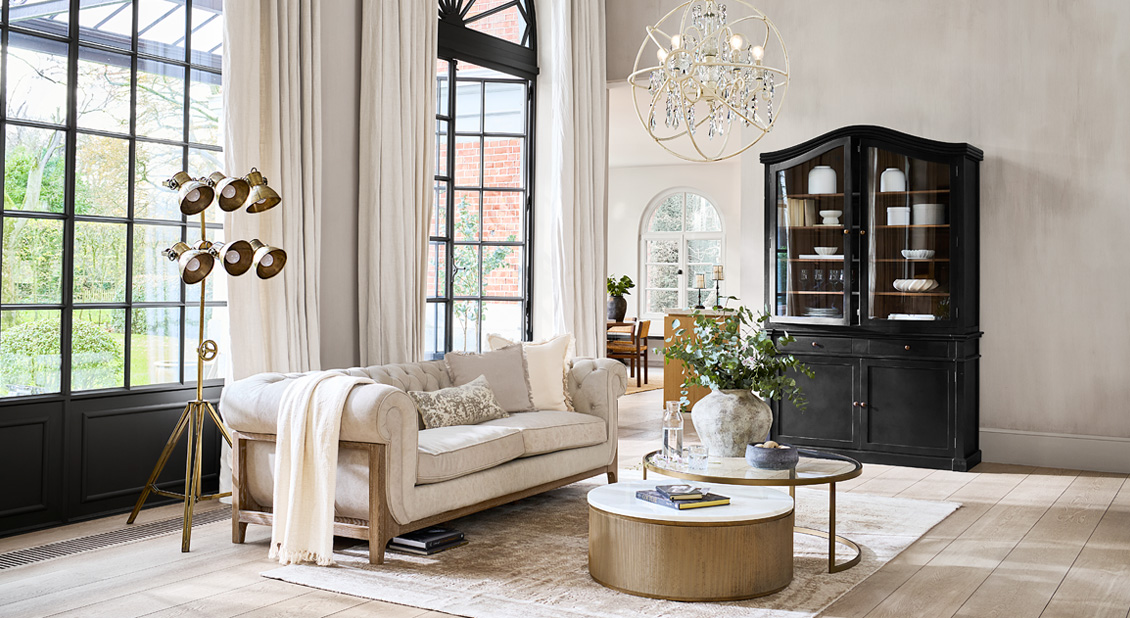 Klassisches beiges Sofa mit Holzrahmen in hellem Wohnzimmer mit schwarzem Vitrinenschrank und Stehlampe