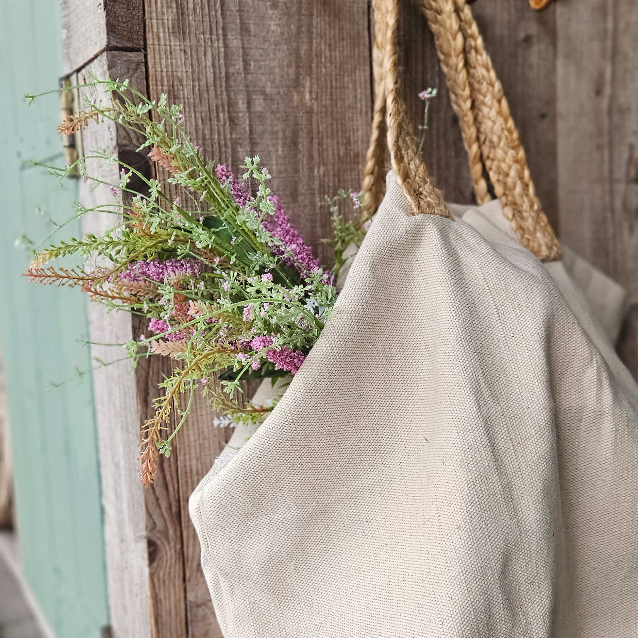 Beige Tasche aus Naturmaterial mit geflochtenen Griffen und Blumen vor rustikalem Holz