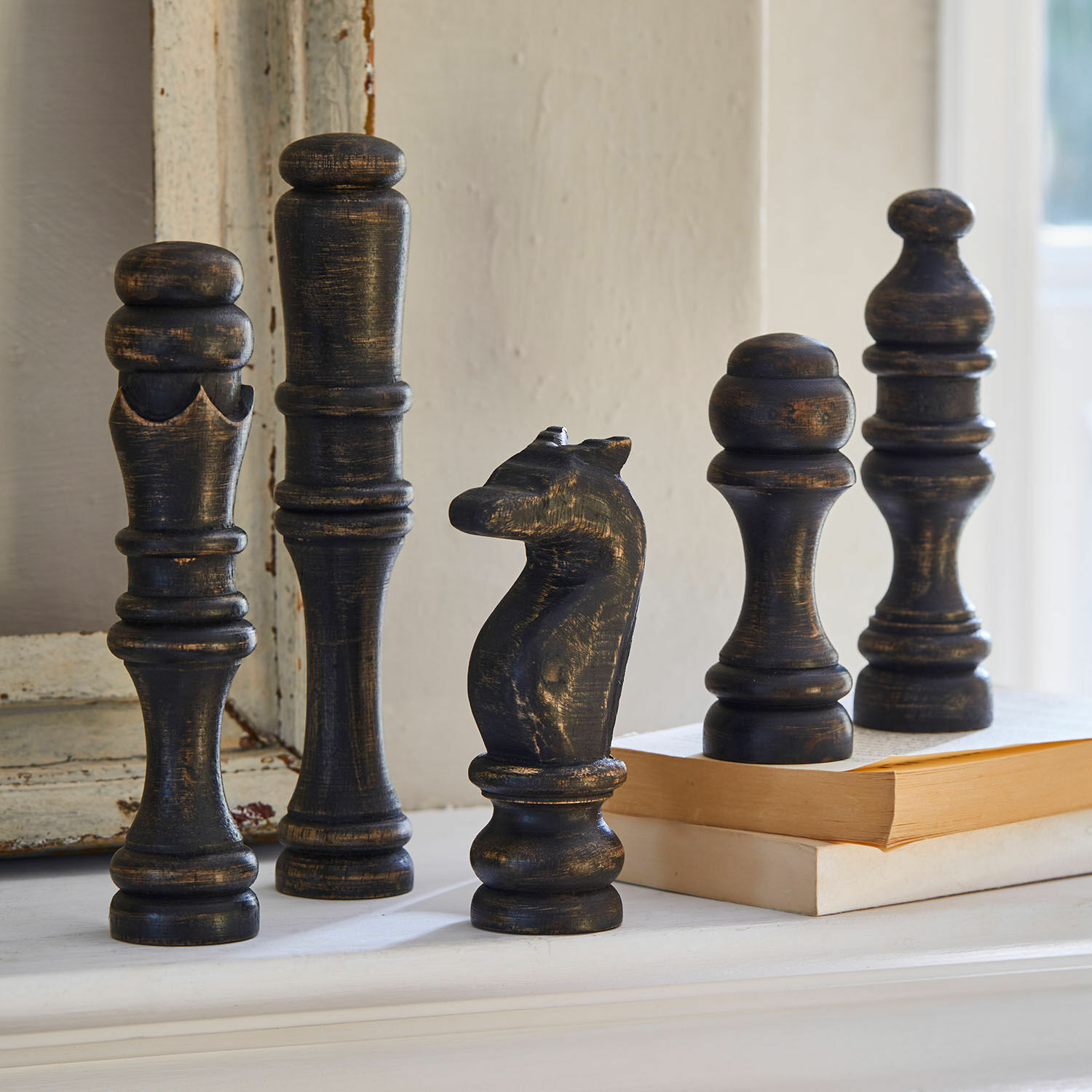 Deko-Objekt 5er Set Guillemineau Dekorative schwarze Holz-Schachfiguren mit antikem Finish auf einem Regal neben Büchern.
