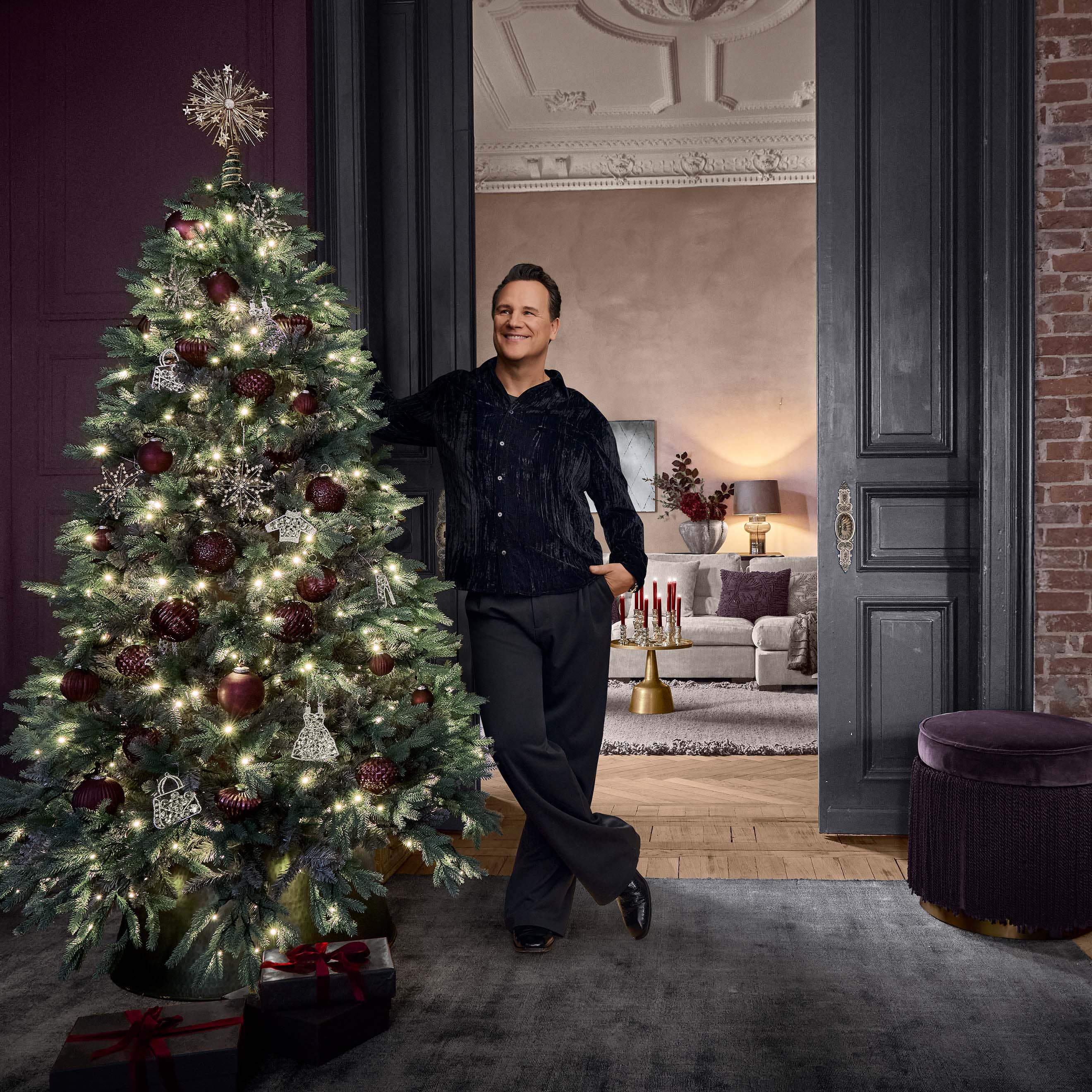 Weihnachtsbaum mit roten und silbernen Kugeln sowie Lichterketten in elegantem Raum mit Mann.