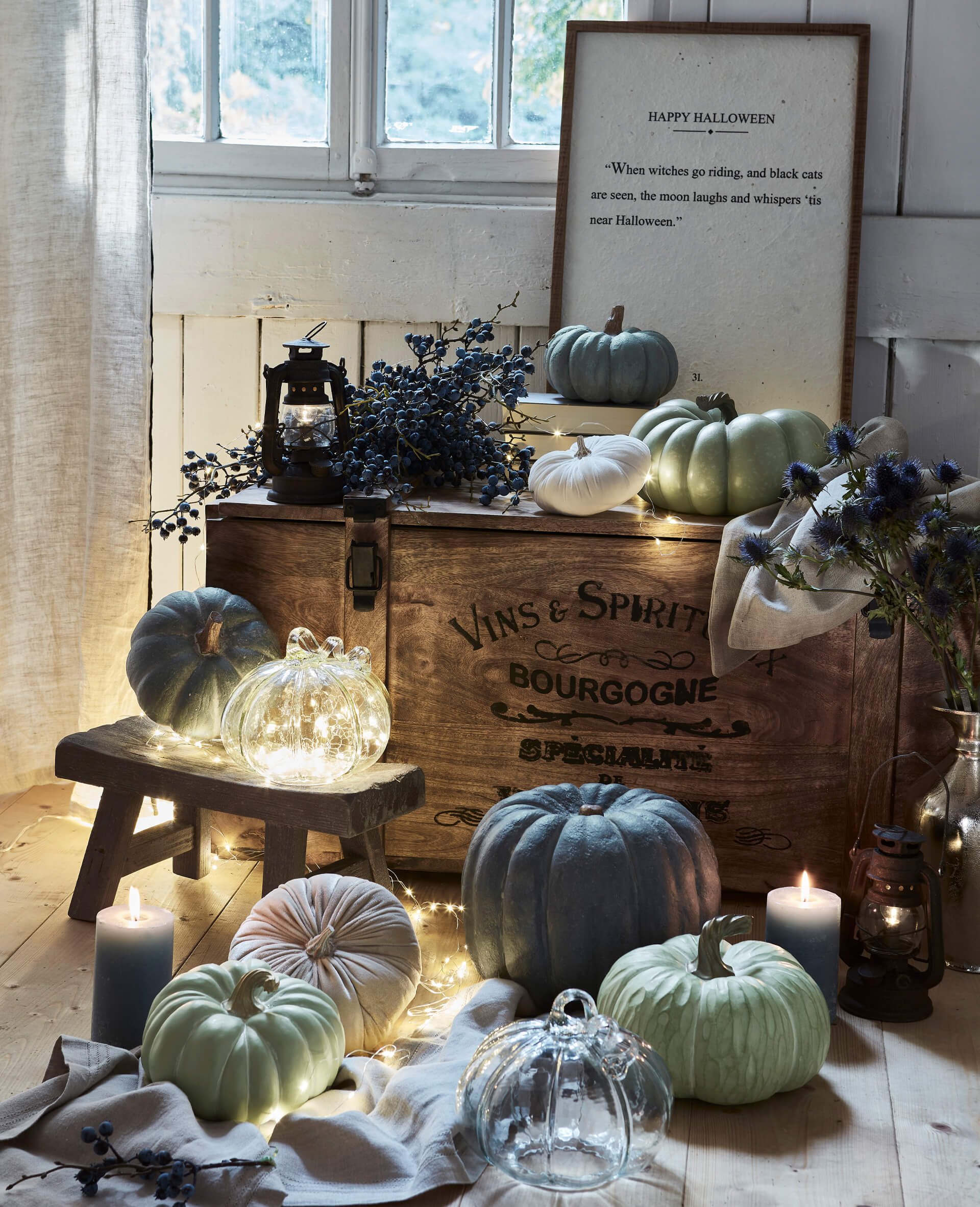 Pastellfarbene Dekorationskürbisse und Glaslaternen auf Holzkiste in herbstlicher Wohnatmosphäre
