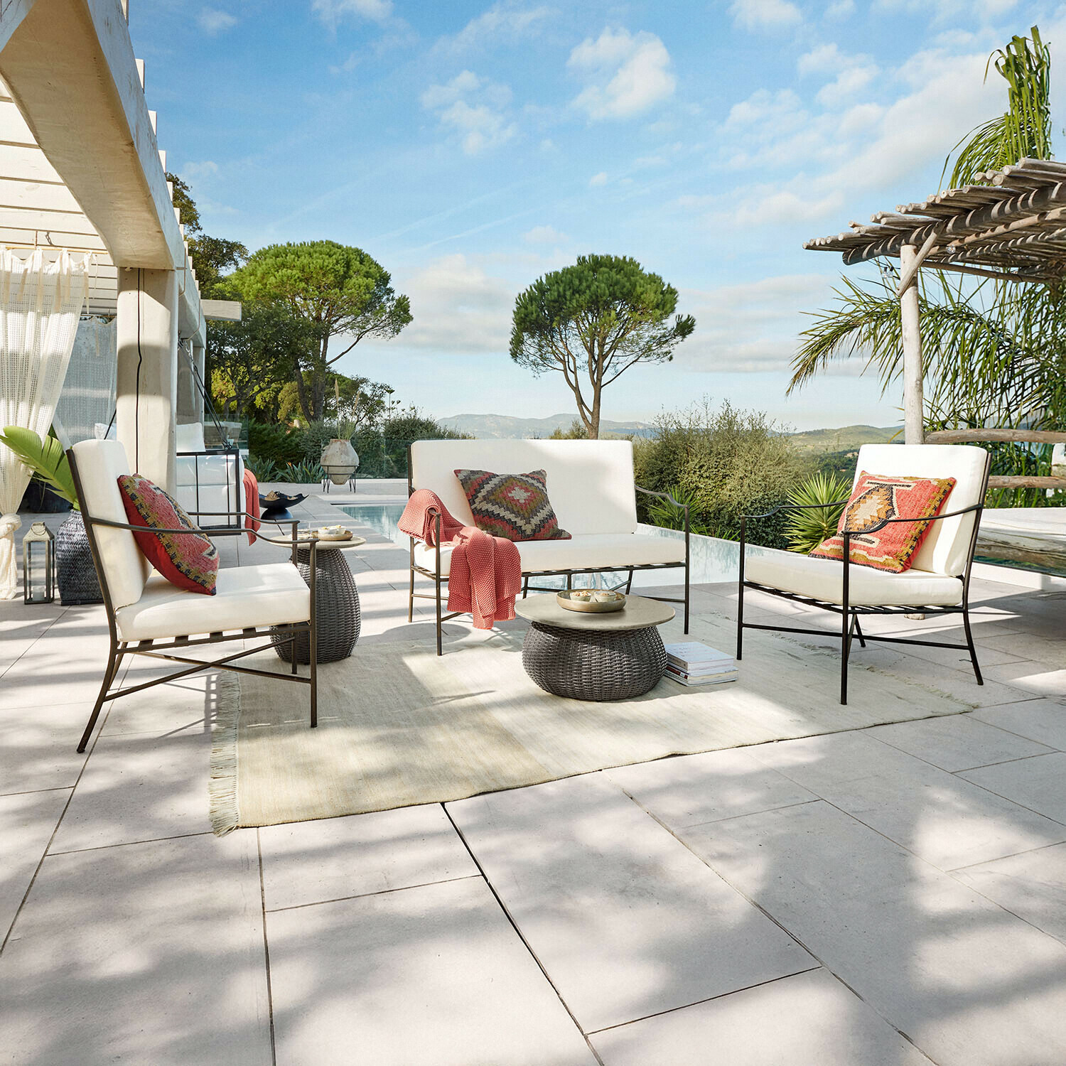 Gartenmöbel-Set mit Metallrahmen und cremefarbenen Polstern auf Terrasse mit Poolblick