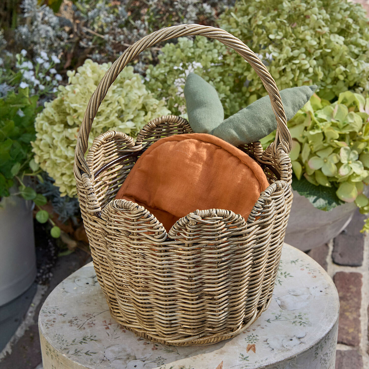 Wikingerkorb mit orangefarbenem Kissen und grünen Blättern, Gartendekoration auf rundem Tisch