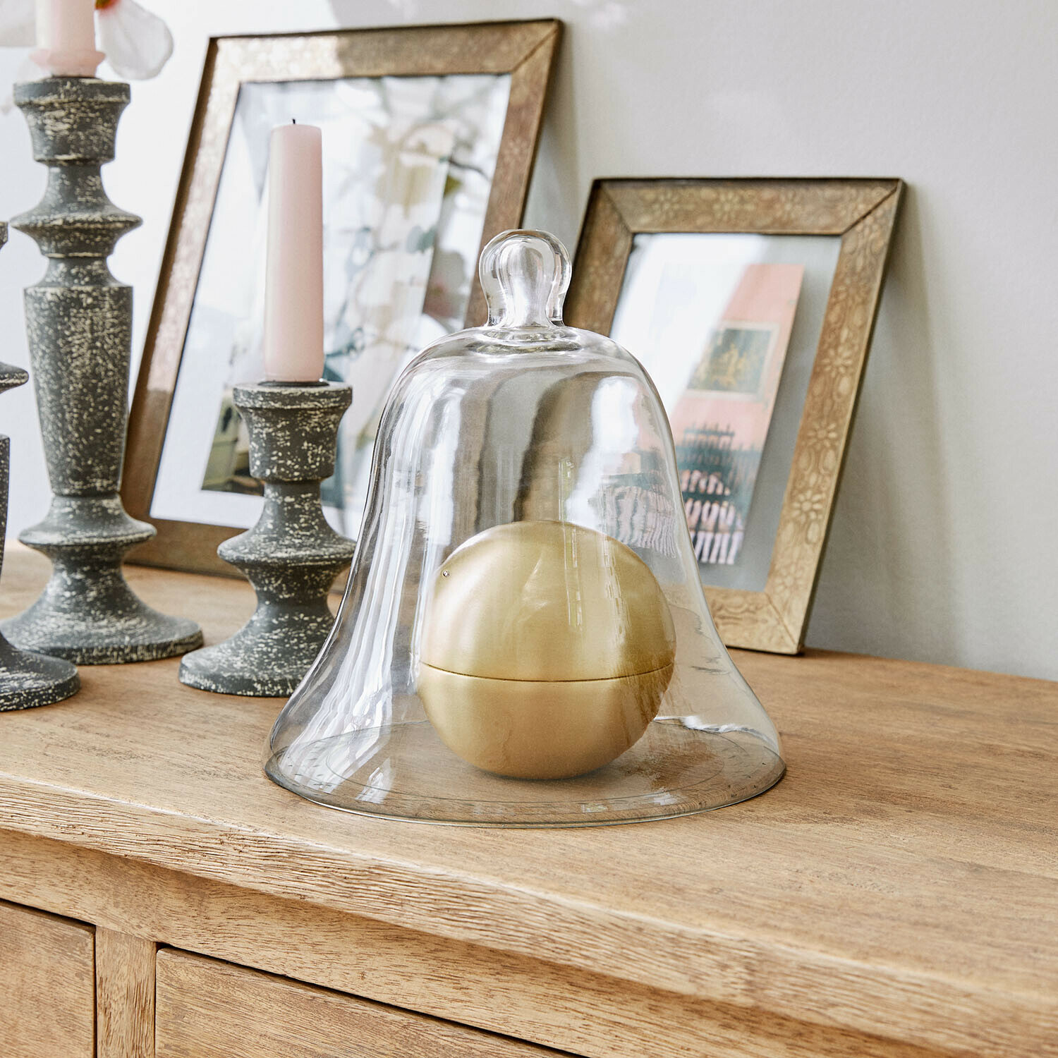 Glasglocke aus klarem Glas mit goldener Kugel auf hellem Holzsideboard dekorativ