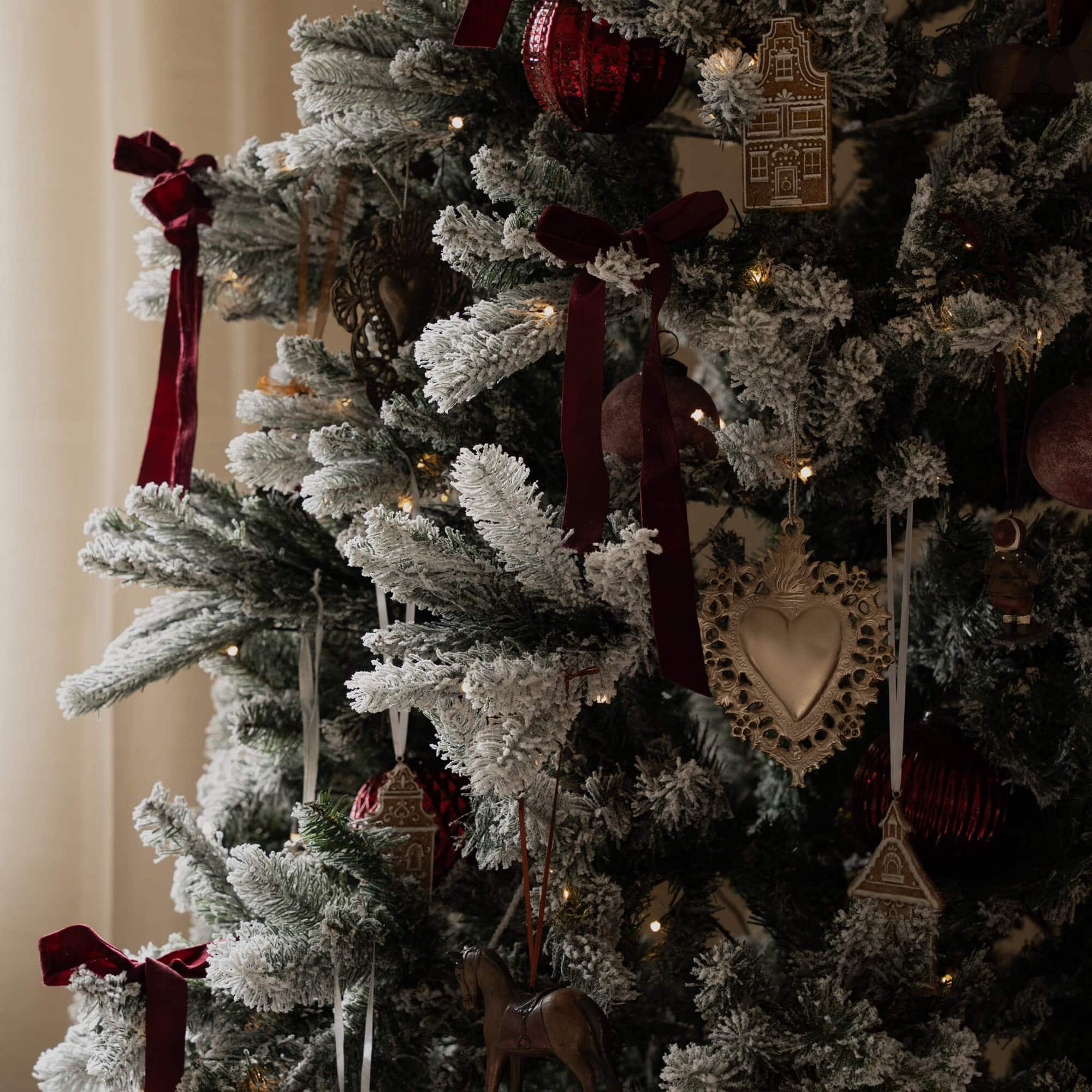 Künstlicher Weihnachtsbaum mit weißem Schneeeffekt, roten Samtbändern und traditionellen Christbaumschmuck